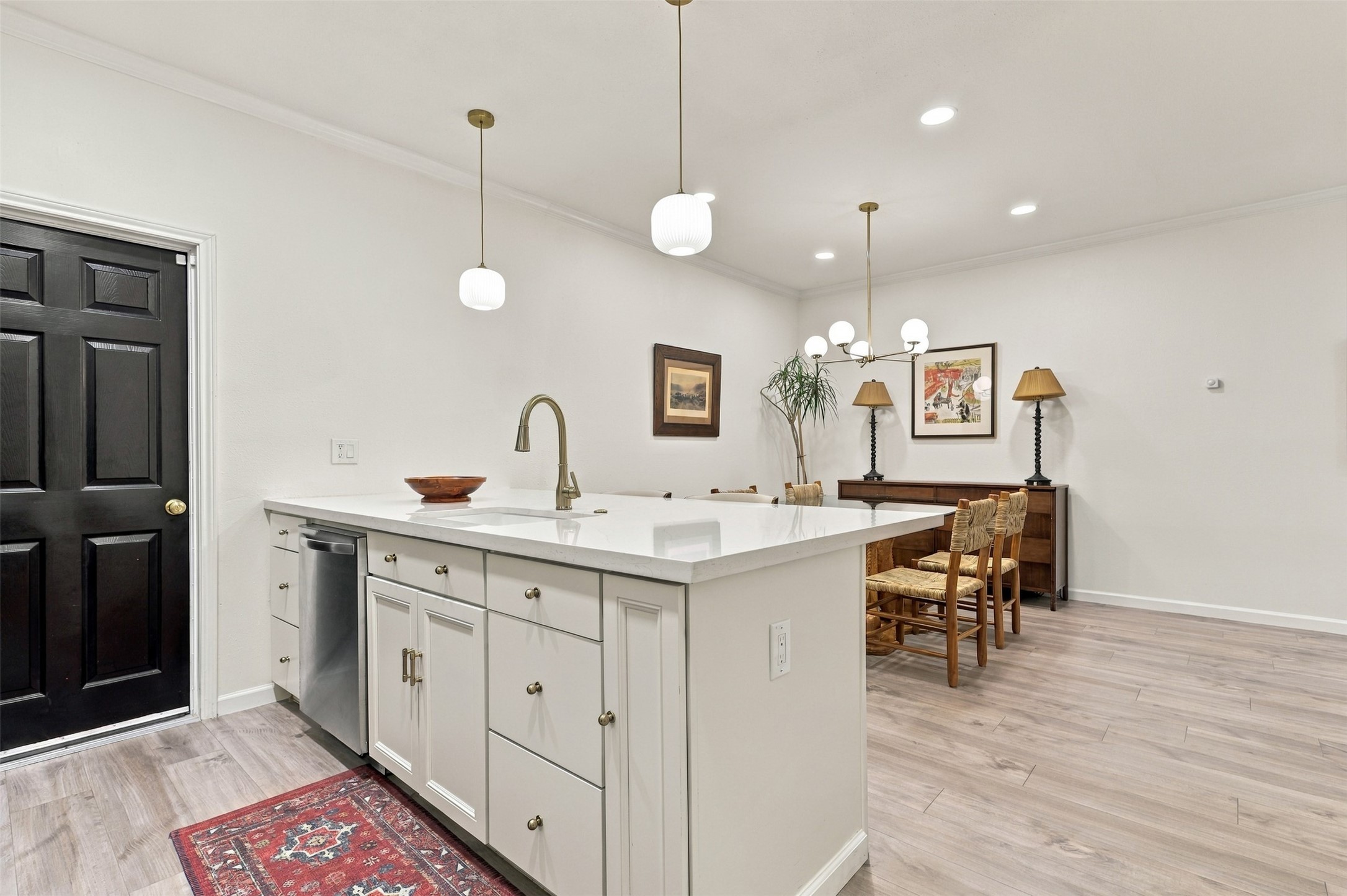Bright and modern kitchen-dining area featuring elegant pendant lighting, a spacious island with a sleek faucet, and stylish cabinetry, seamlessly connected to an inviting dining space with tasteful decor.