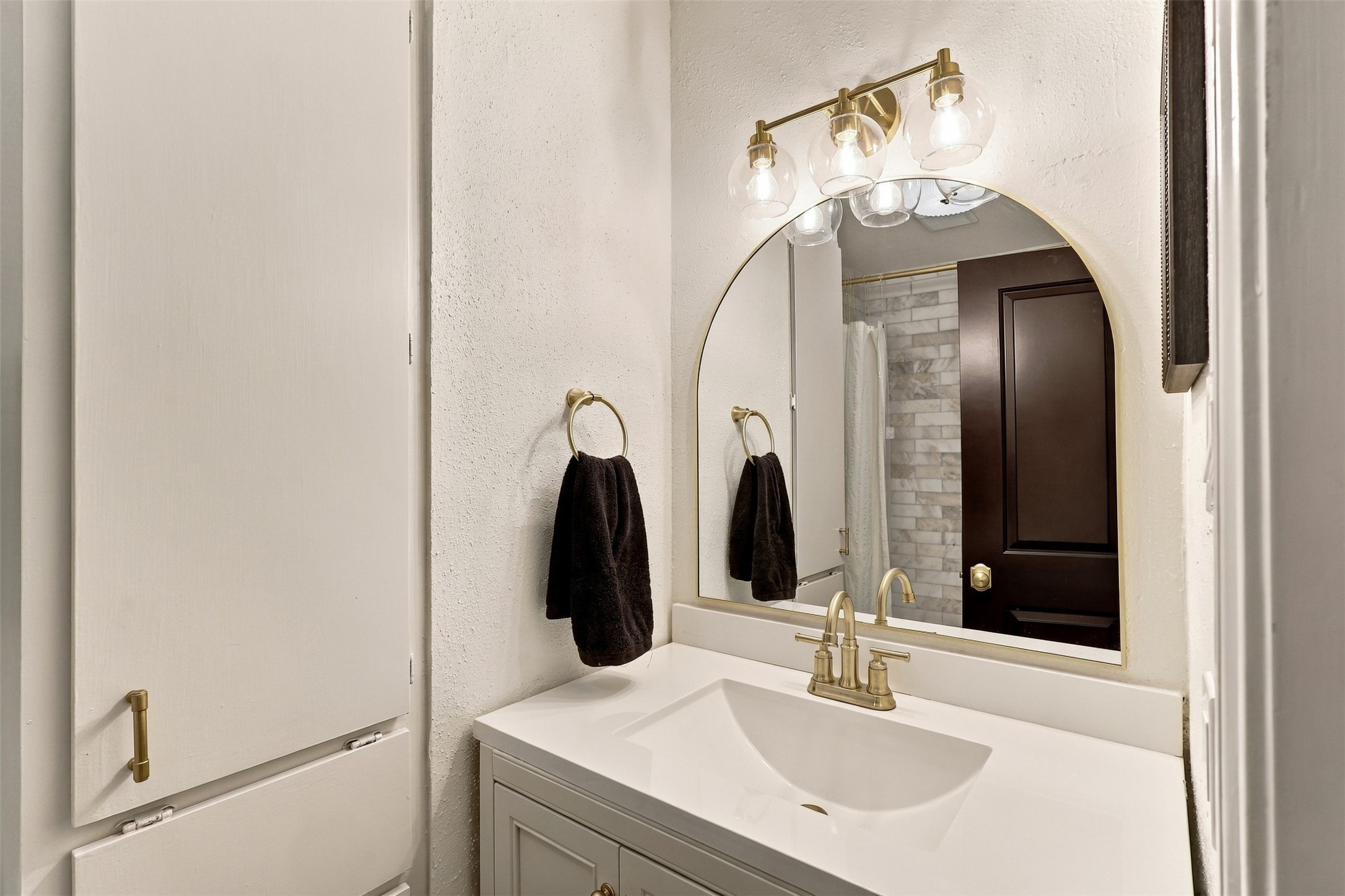 Elegant bathroom featuring a modern vanity with a sleek countertop, complemented by a stylish arched mirror and chic lighting fixtures.