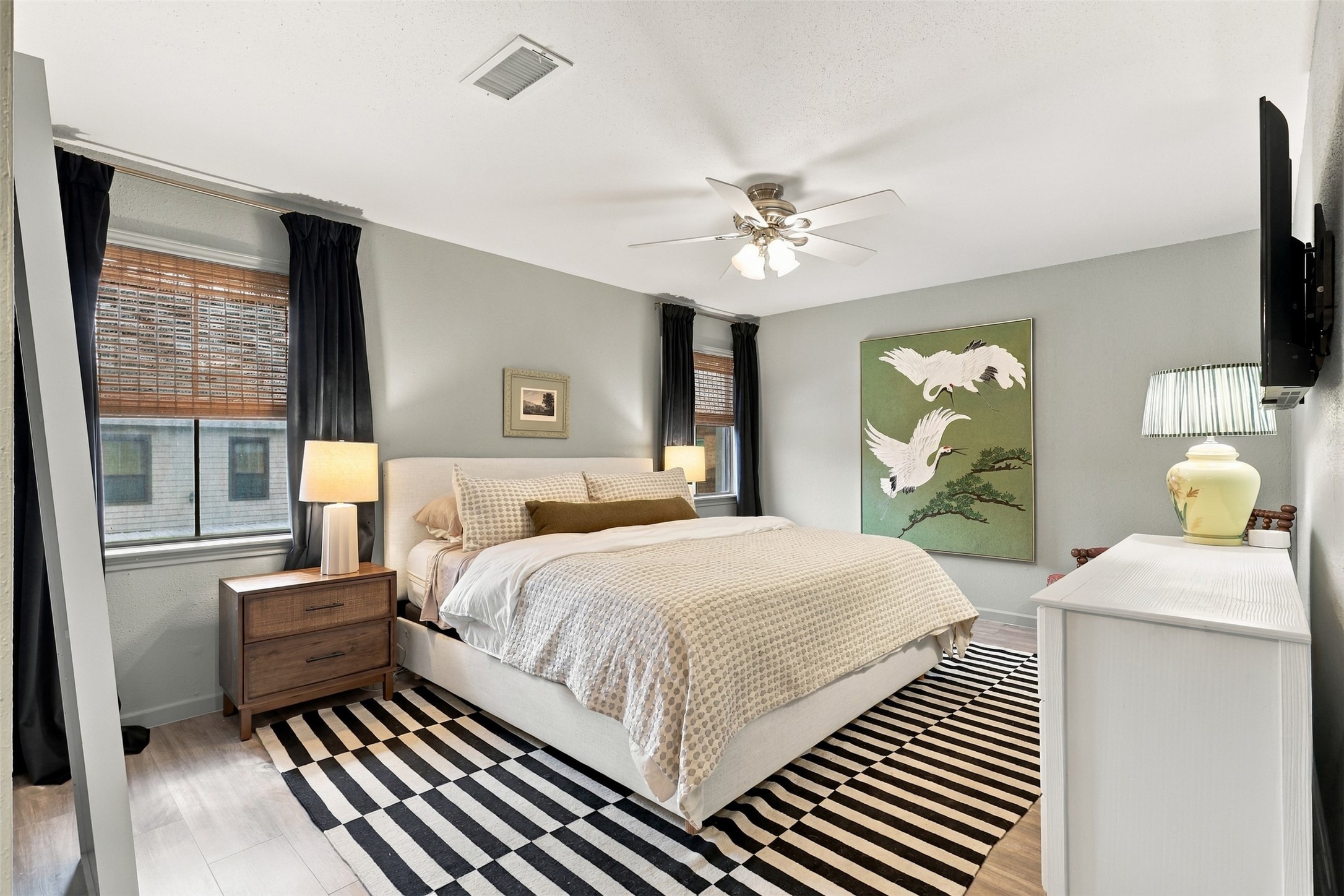 A cozy bedroom featuring a plush bed, modern decor, and ample natural light, complemented by stylish art and elegant furnishings.