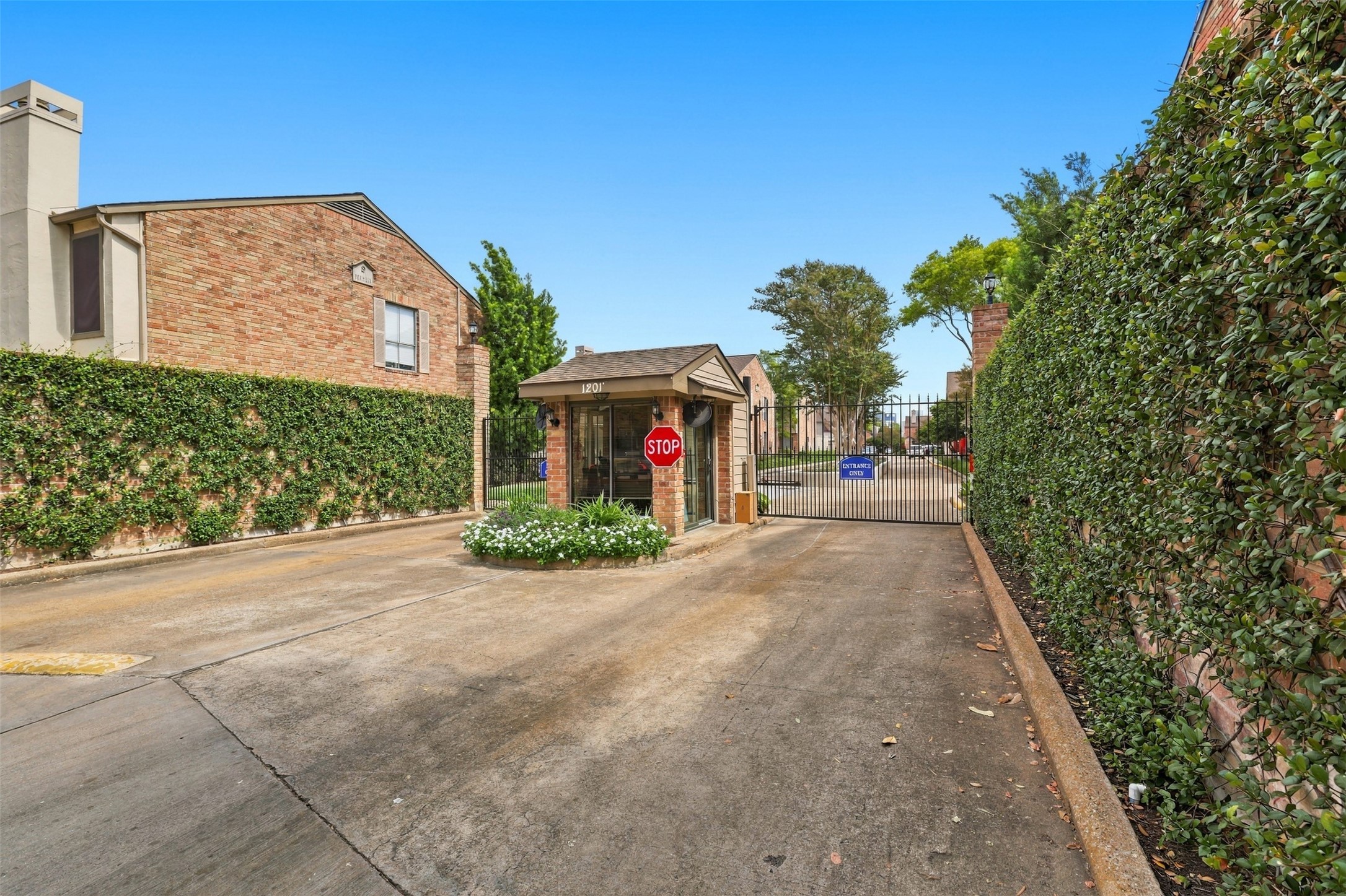 Gated community entrance featuring lush greenery and a welcoming security booth, providing privacy and peace of mind.