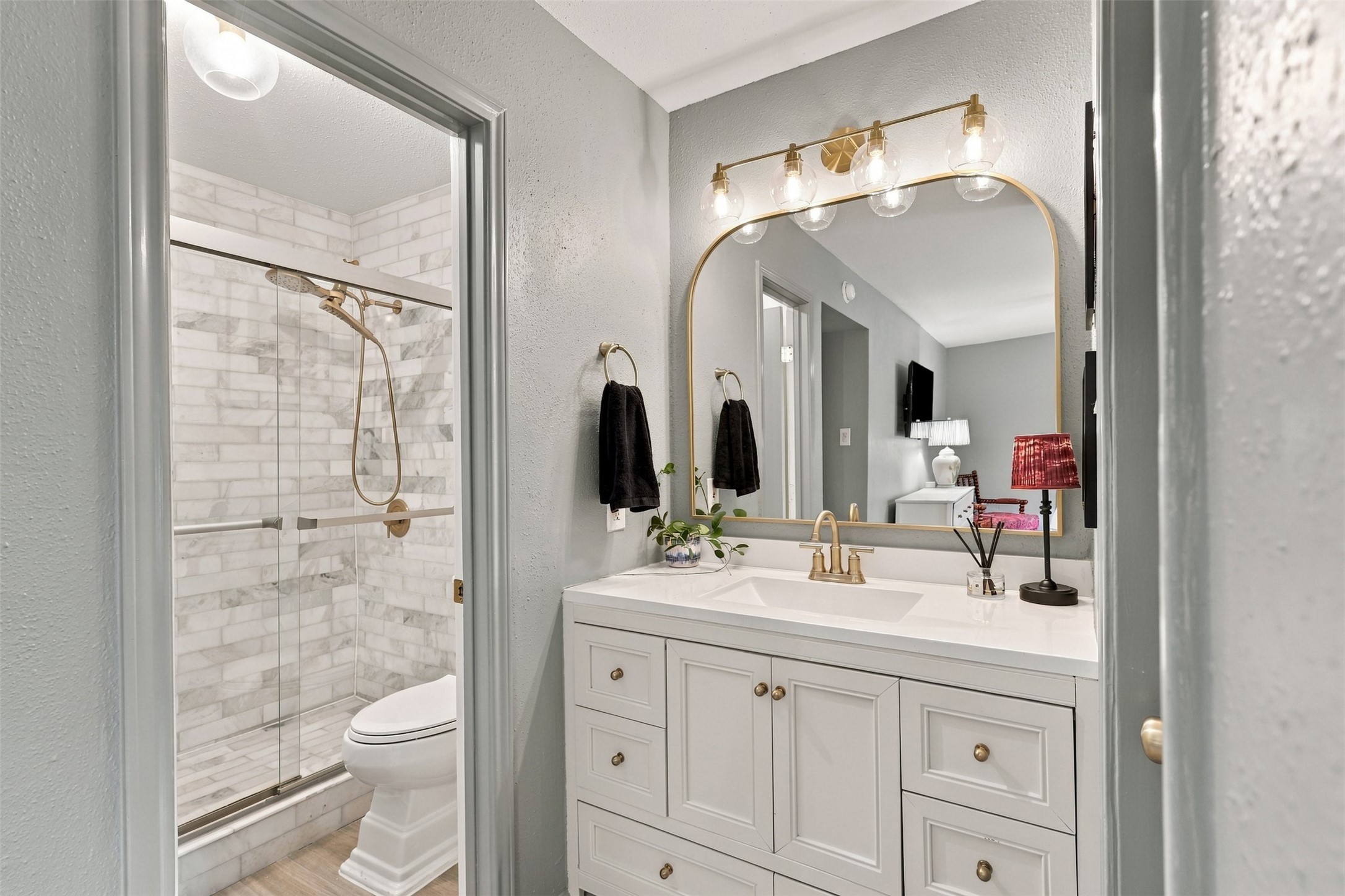 Elegant bathroom featuring a stylish vanity with a gold-framed mirror, modern light fixtures, and a glass-enclosed marble shower.