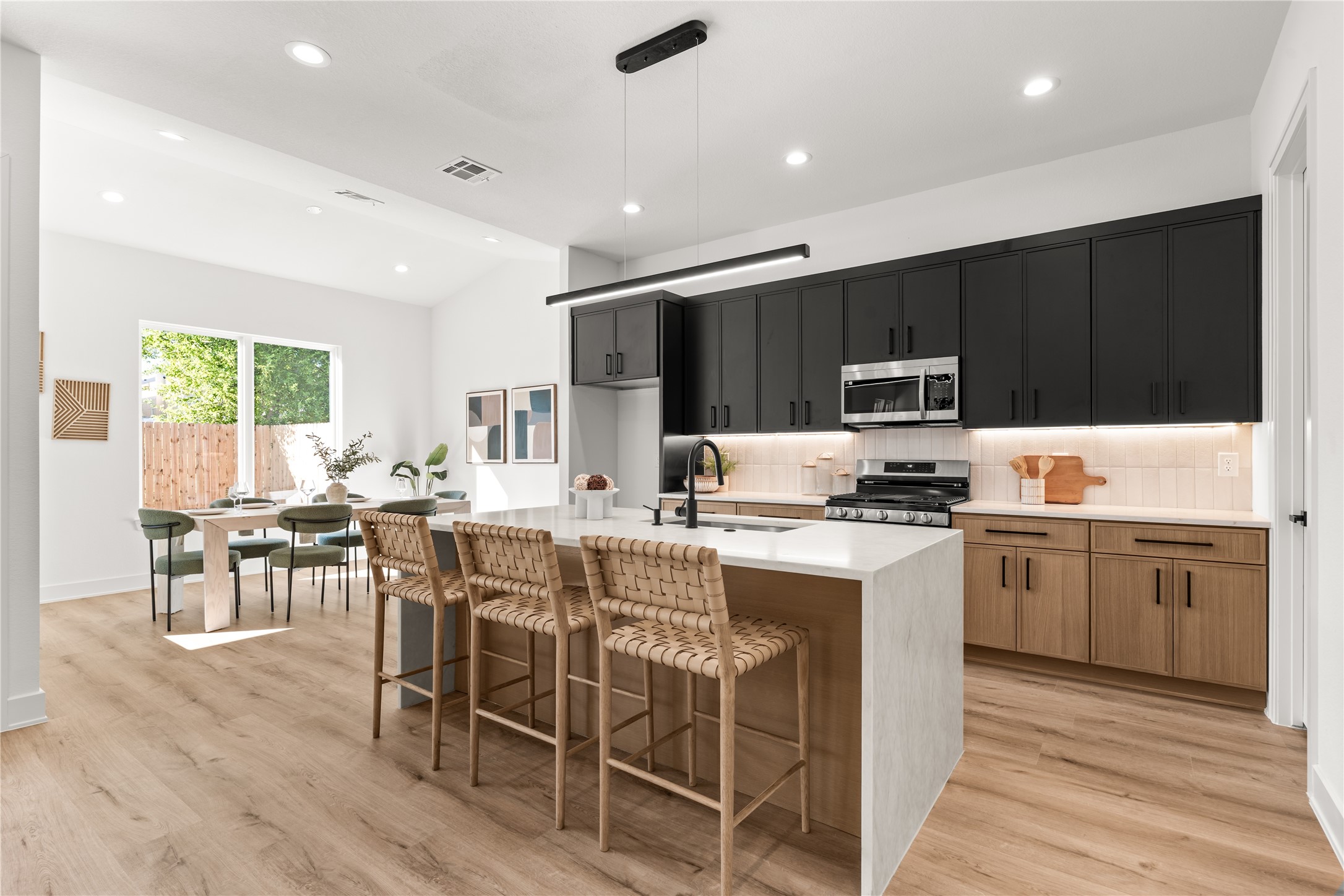 Nima Homes' attention to detail is reflected in the kitchen's layered material palette, from vertically stacked backsplash tile and illuminated countertops to sleek black hardware and contrasting cabinetry.