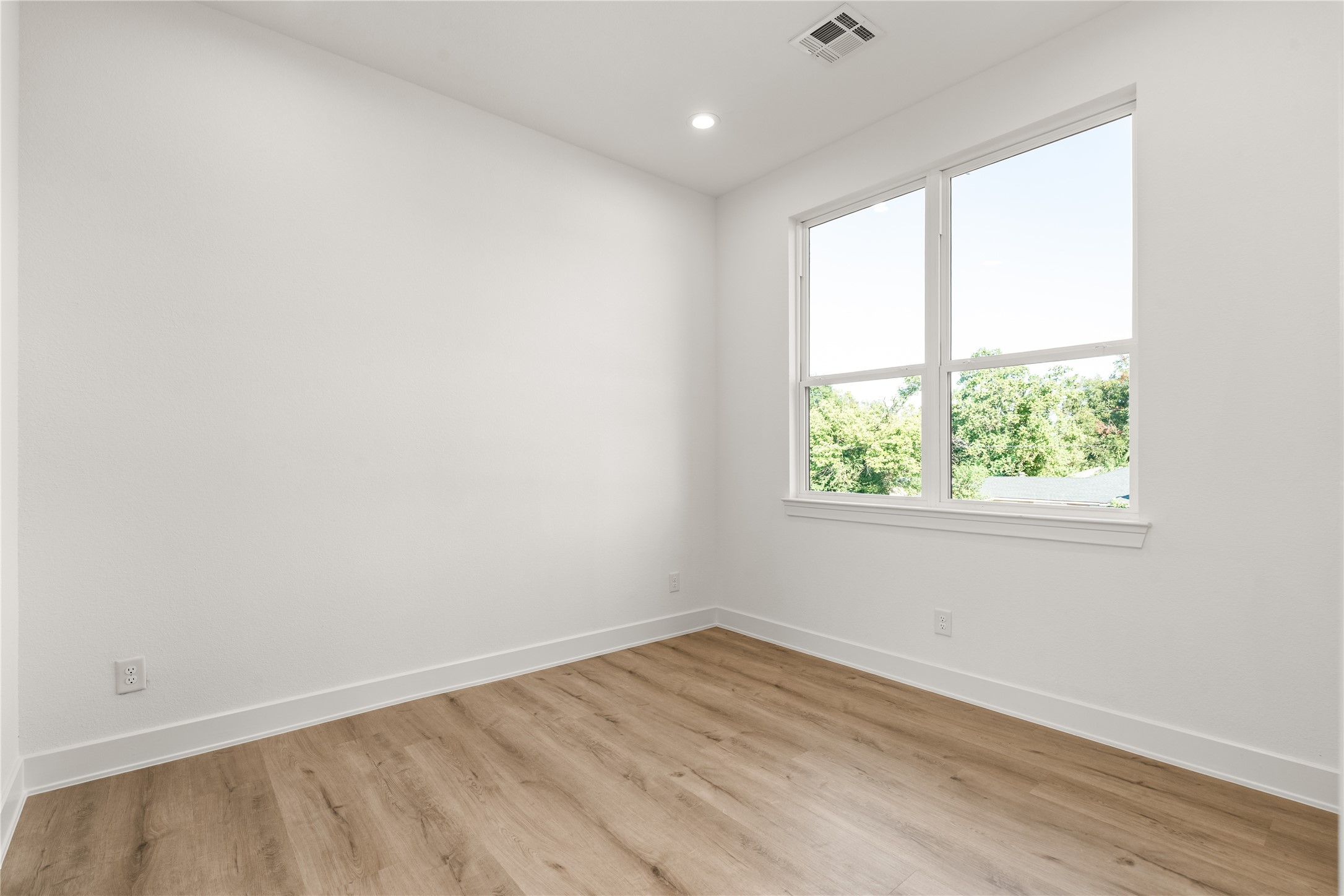 A large window frames this secondary bedroom with views of the surrounding greenery, bringing an inviting connection to the outdoors.