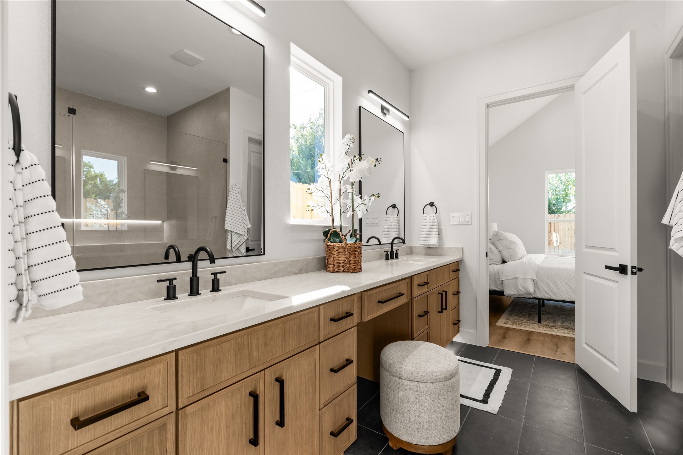 Spanning the length of the primary ensuite, the dual-sink vanity showcases warm cabinetry accented by matte black hardware and sleek surfaces.
