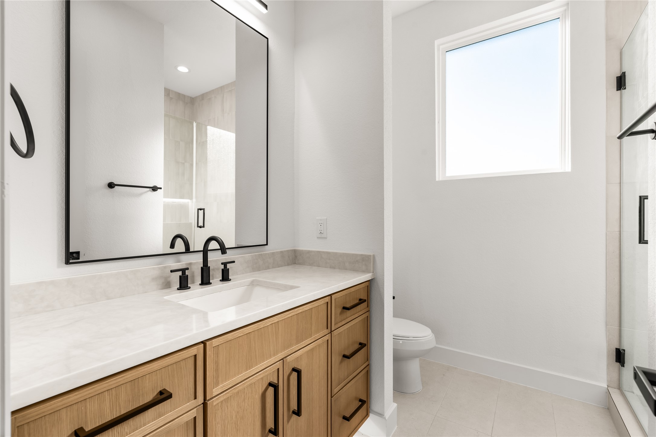 Designed with both practicality and visual appeal in mind, this private en suite features an expansive vanity with ample storage, a glass-enclosed shower, and a contemporary selection of finishes.