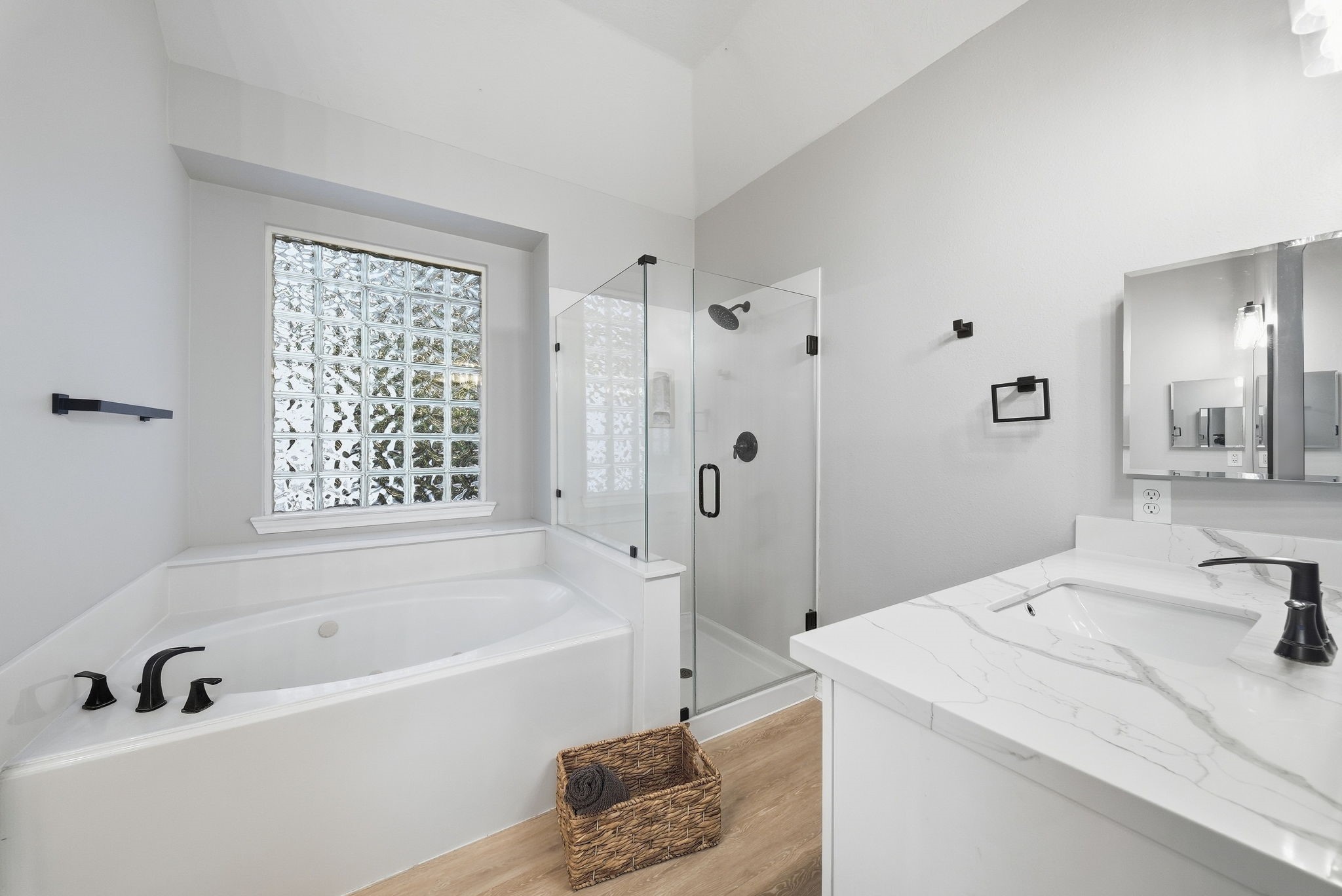 Spacious bathroom with soaking tub, glass-enclosed walk-in shower, quartz vanity, and glass block window.