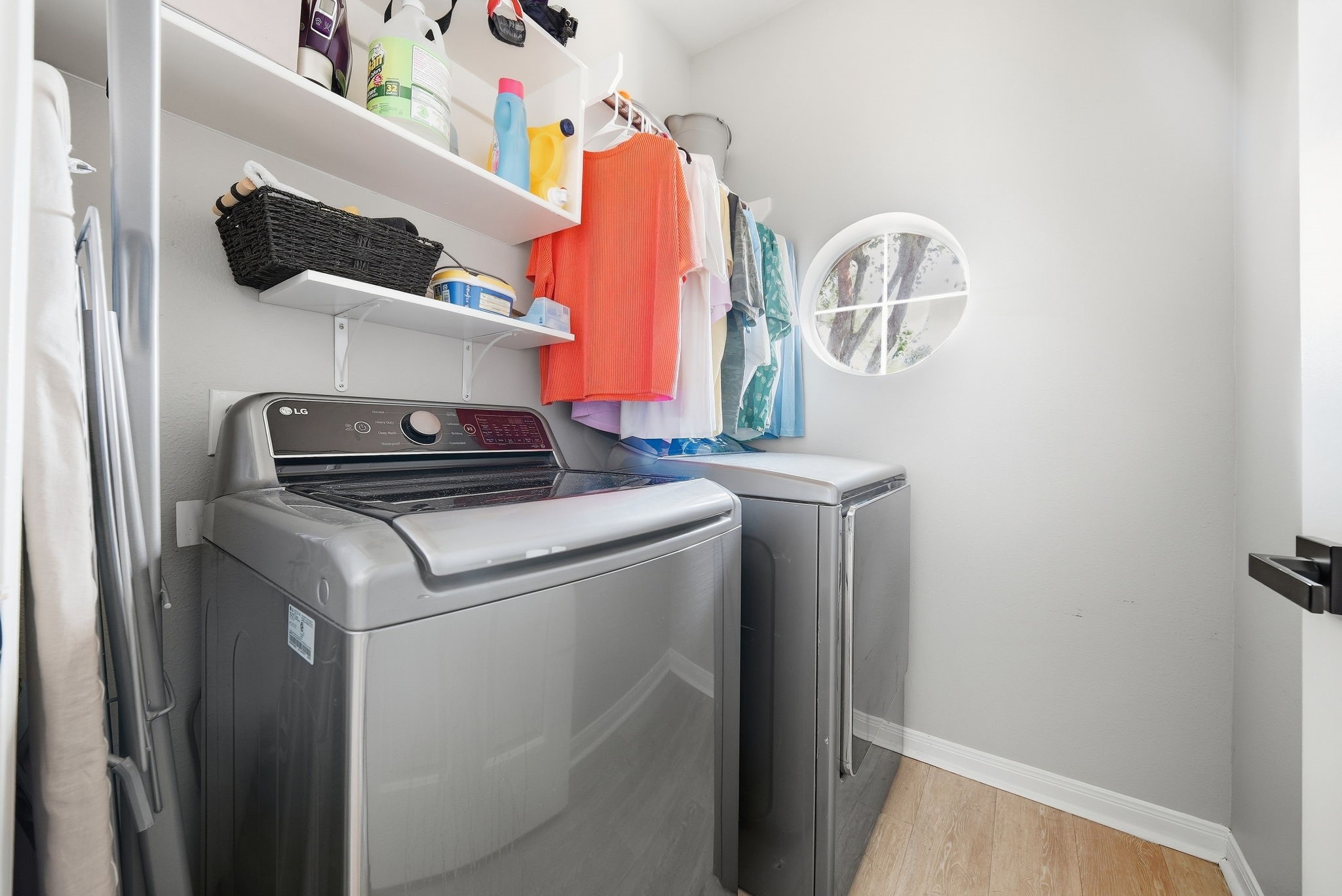 Convenient laundry room with a washer and dryer, built-in shelving, hanging space, and a round window for natural light.
