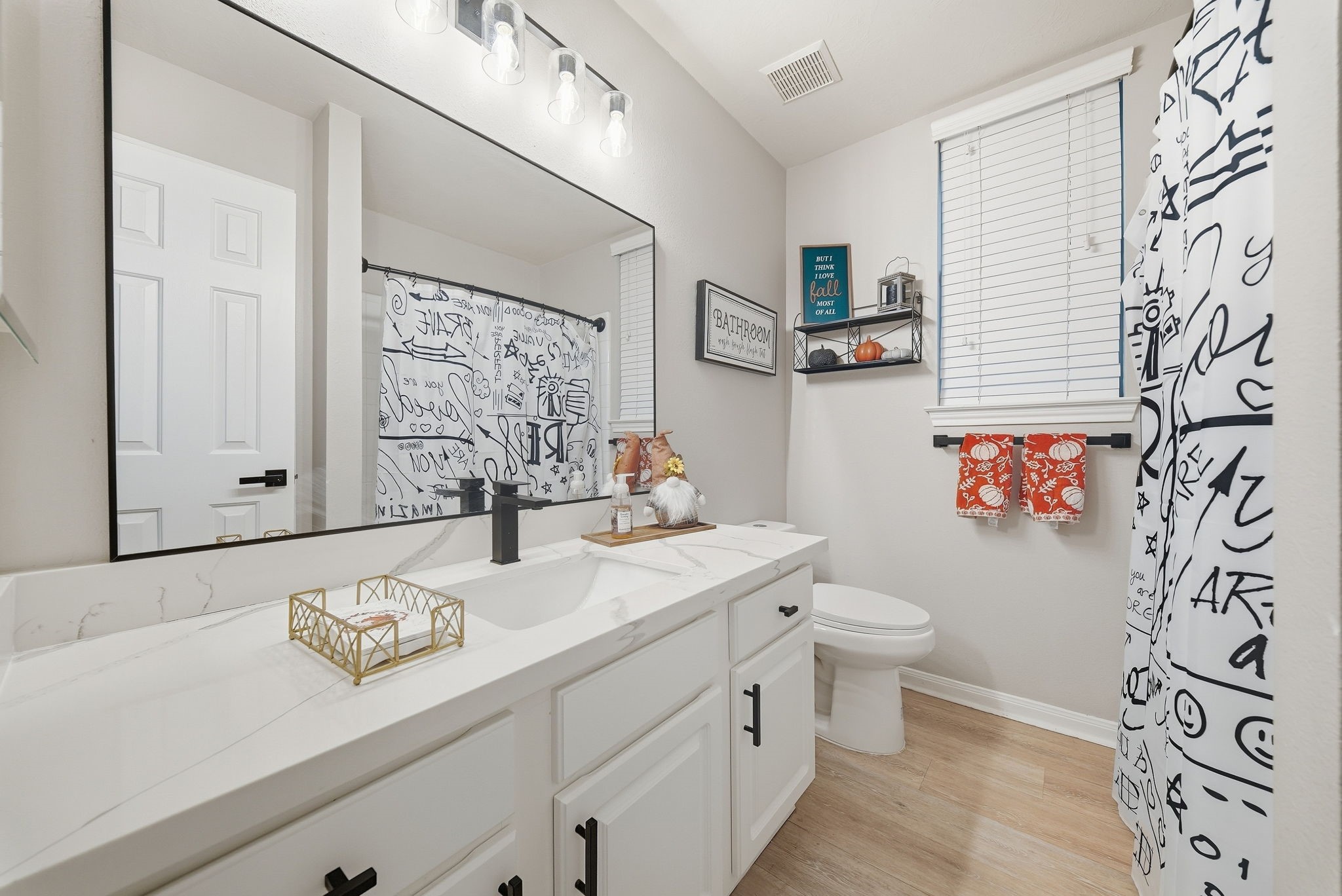 Updated bathroom with quartz vanity, large framed mirror, black fixtures, and glass-enclosed shower with patterned curtain.