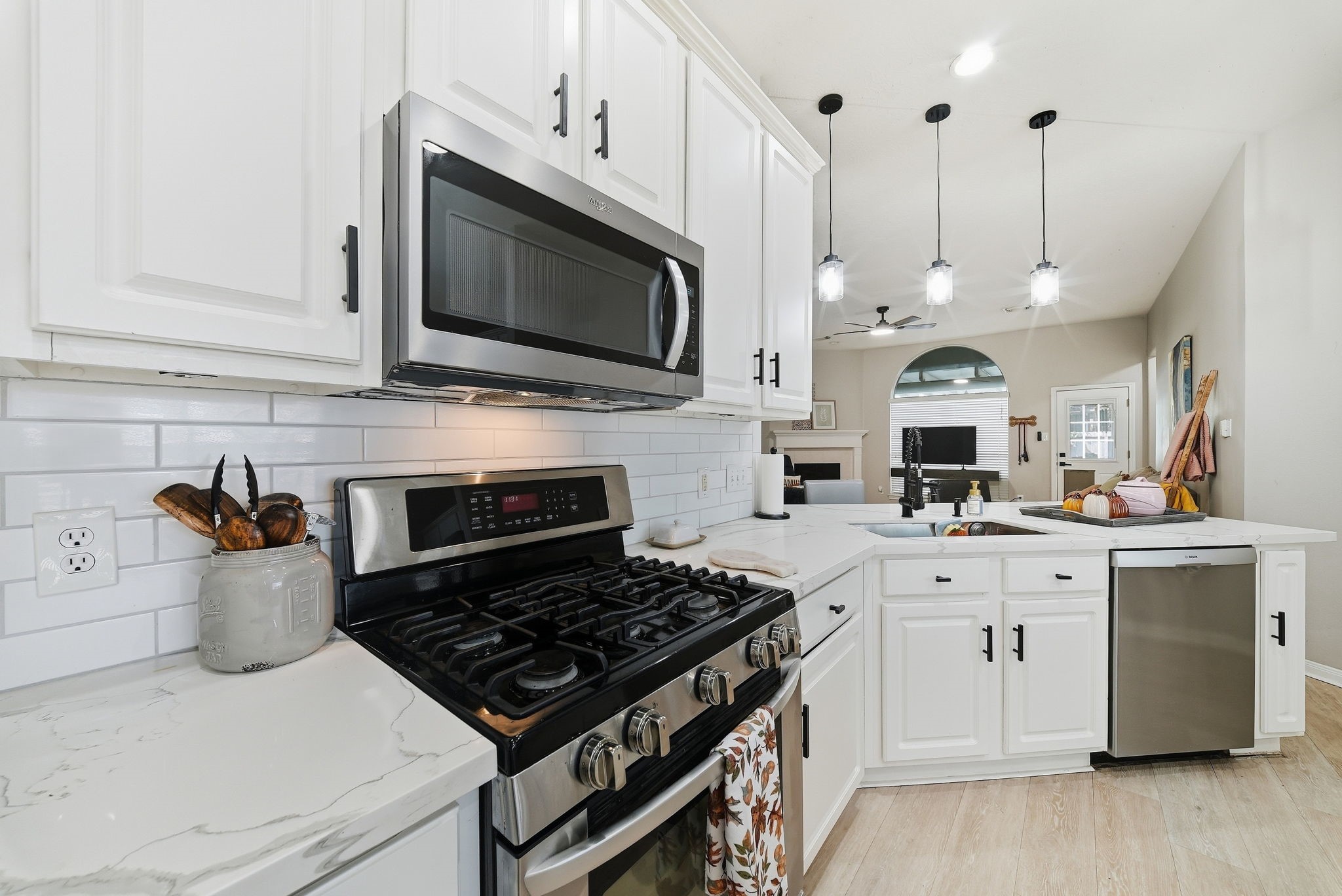 Updated kitchen with gas range, built-in microwave, white cabinetry, quartz countertops, subway tile backsplash, and stainless steel dishwasher.