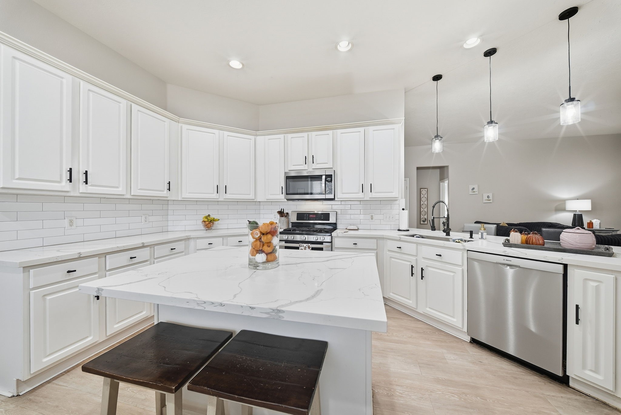 Spacious kitchen featuring white cabinetry, quartz countertops, large center island, stainless steel appliances, and pendant lighting.