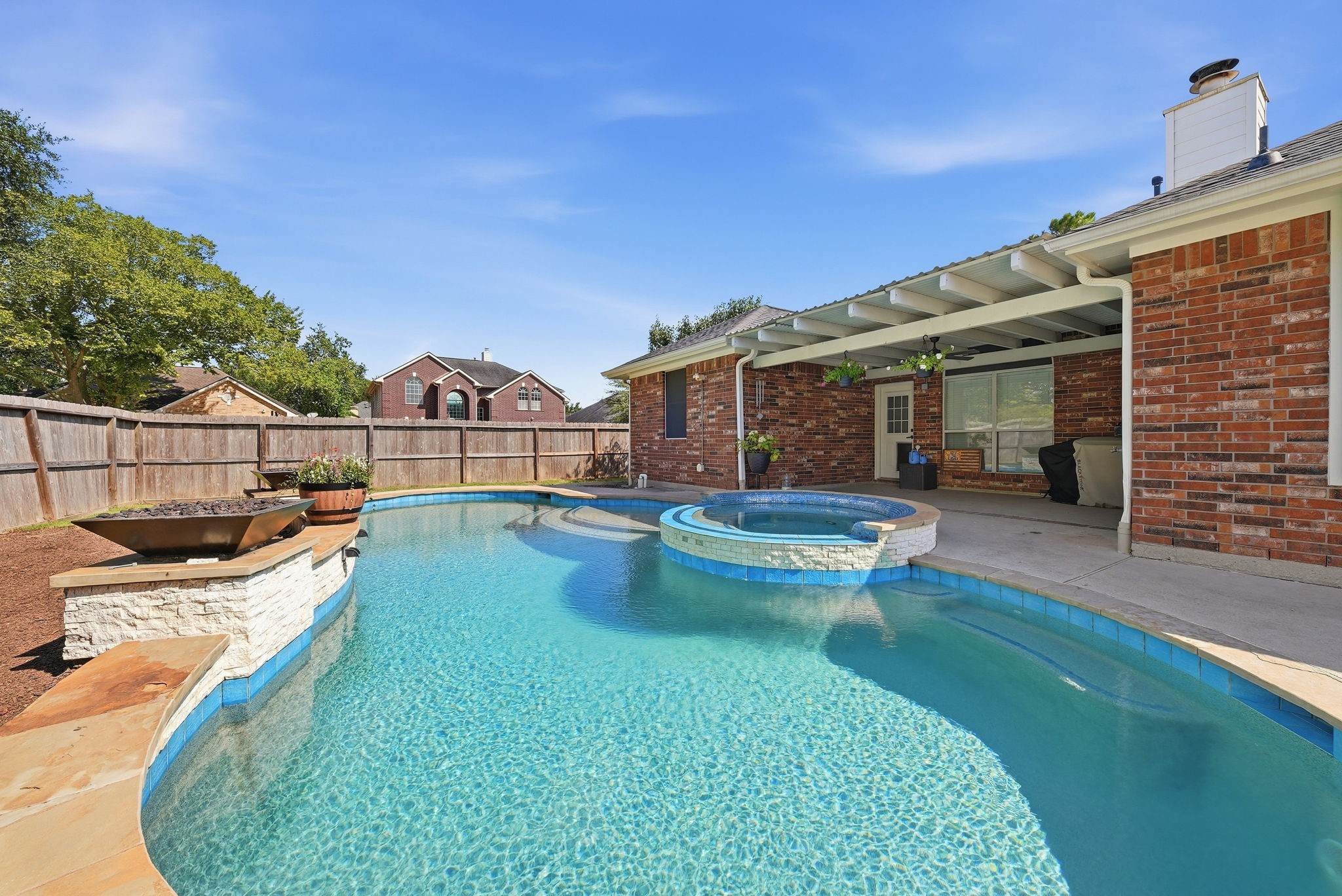 Expansive backyard pool with raised spa, covered patio, brick exterior, and fenced yard.