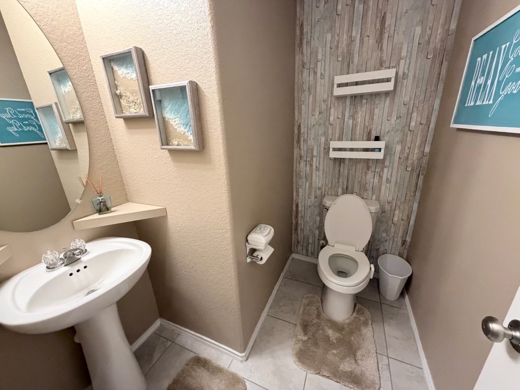 This bathroom features a clean, modern design with neutral tones. It includes a pedestal sink, a toilet with a rustic wood accent wall that is designed for comfort.