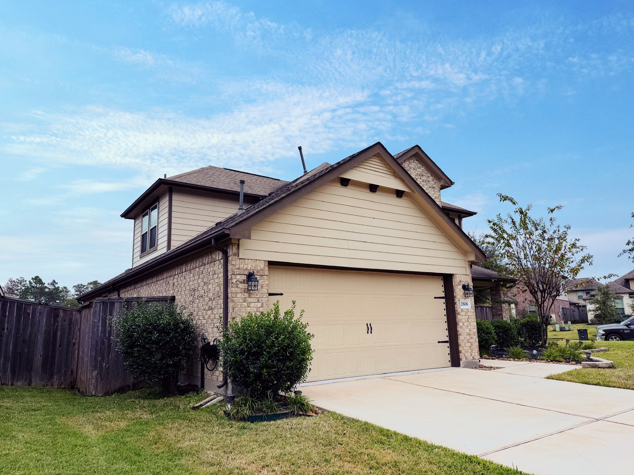 This photo features a modern two-story smart home with a brick facade and beige siding. It has a double garage, well-maintained lawn, and is situated in a suburban neighborhood. The driveway and landscaping enhance its curb appeal.