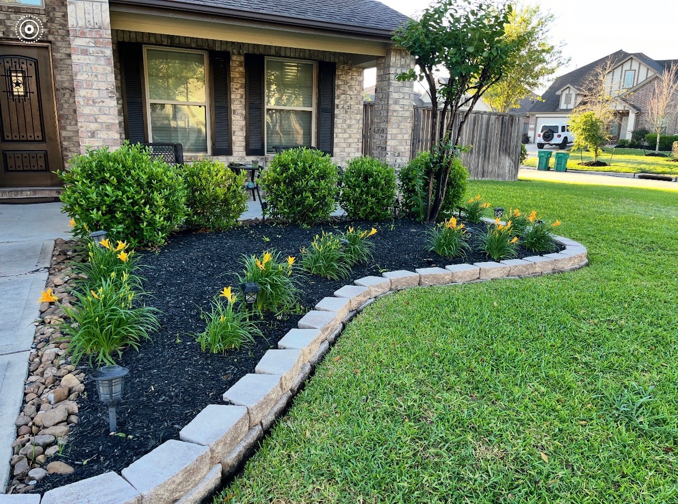 Charming home with a well-maintained front yard featuring a brick facade, lush green lawn, and a beautifully landscaped garden bed with vibrant flowers and shrubs, lined with stone edging.