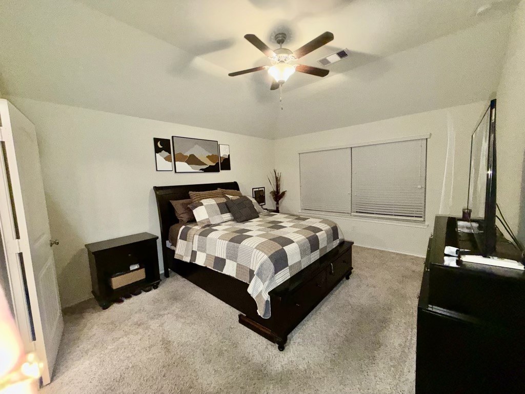 Experience comfort and style in this spacious 13x15 primary suite, featuring a cozy, carpeted floor, modern ceiling fan, and ample natural light.