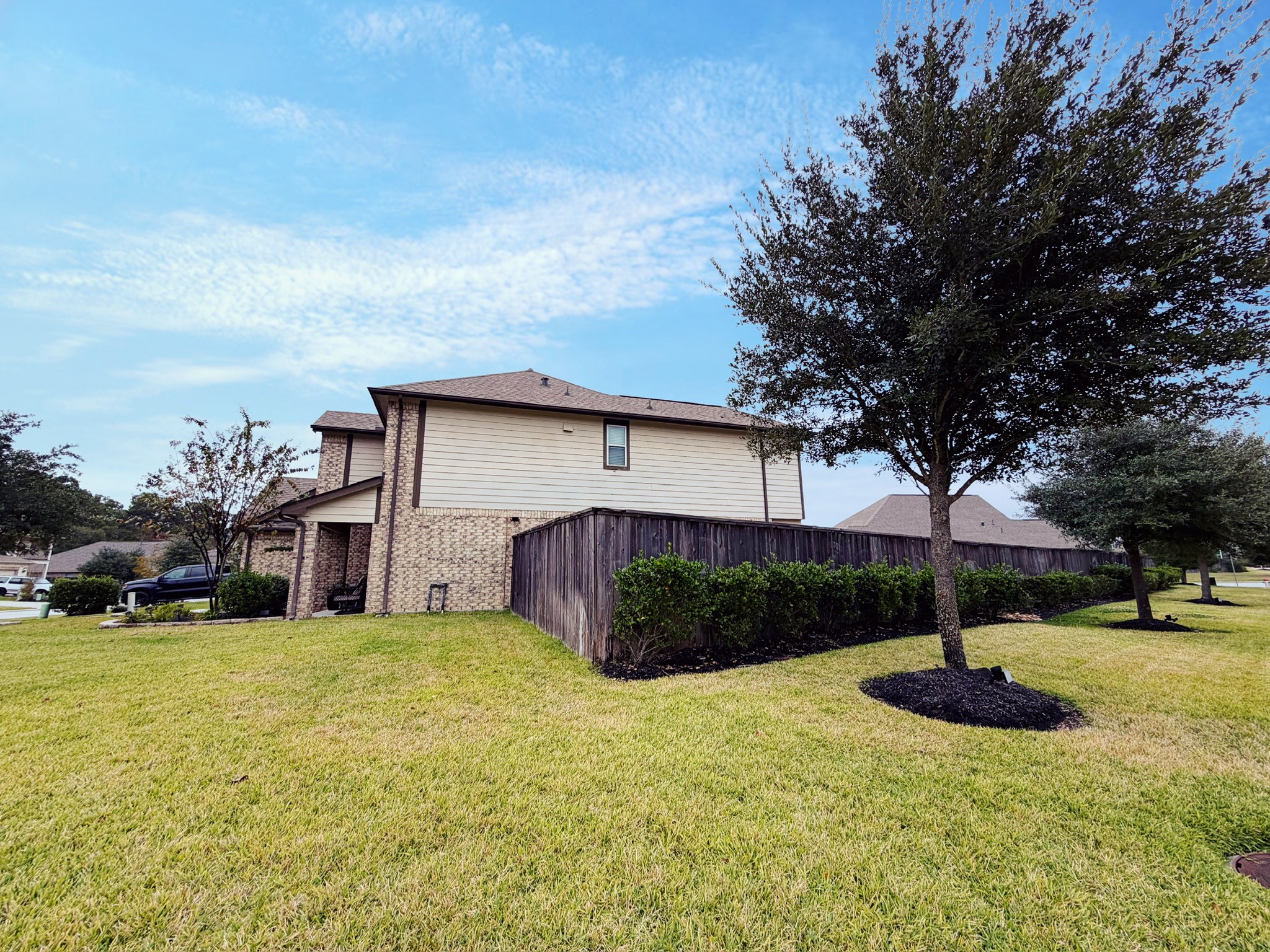 This photo shows a two-story brick and siding house with a well-maintained lawn and surrounding trees, offering a spacious corner lot with ample greenery.