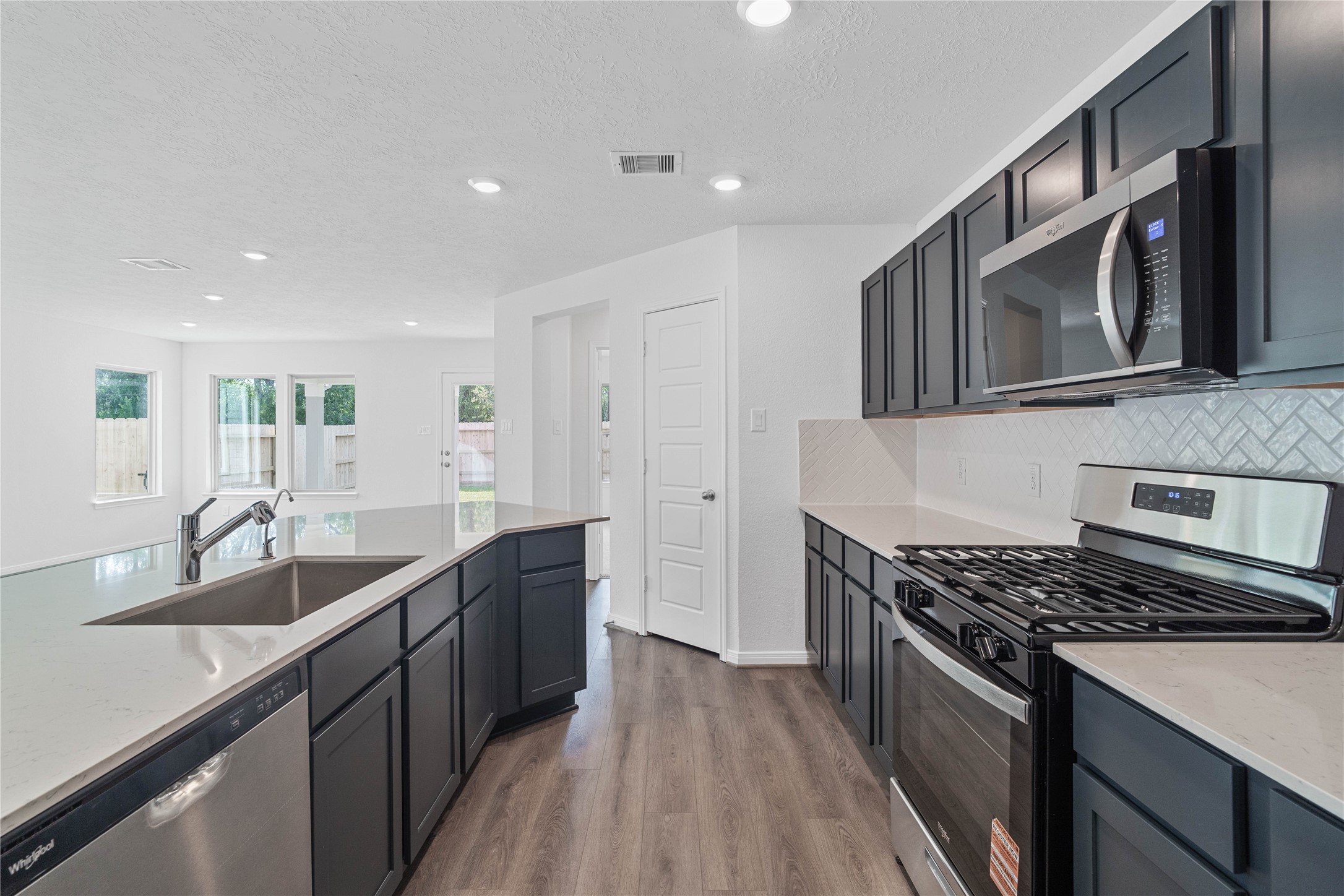 This bright, open kitchen is a chef's delight, complete with a large island, quartz countertops, stained Woodmont Dakota cabinets, Whirlpool stainless steel appliances, and modern Daltile backsplash.