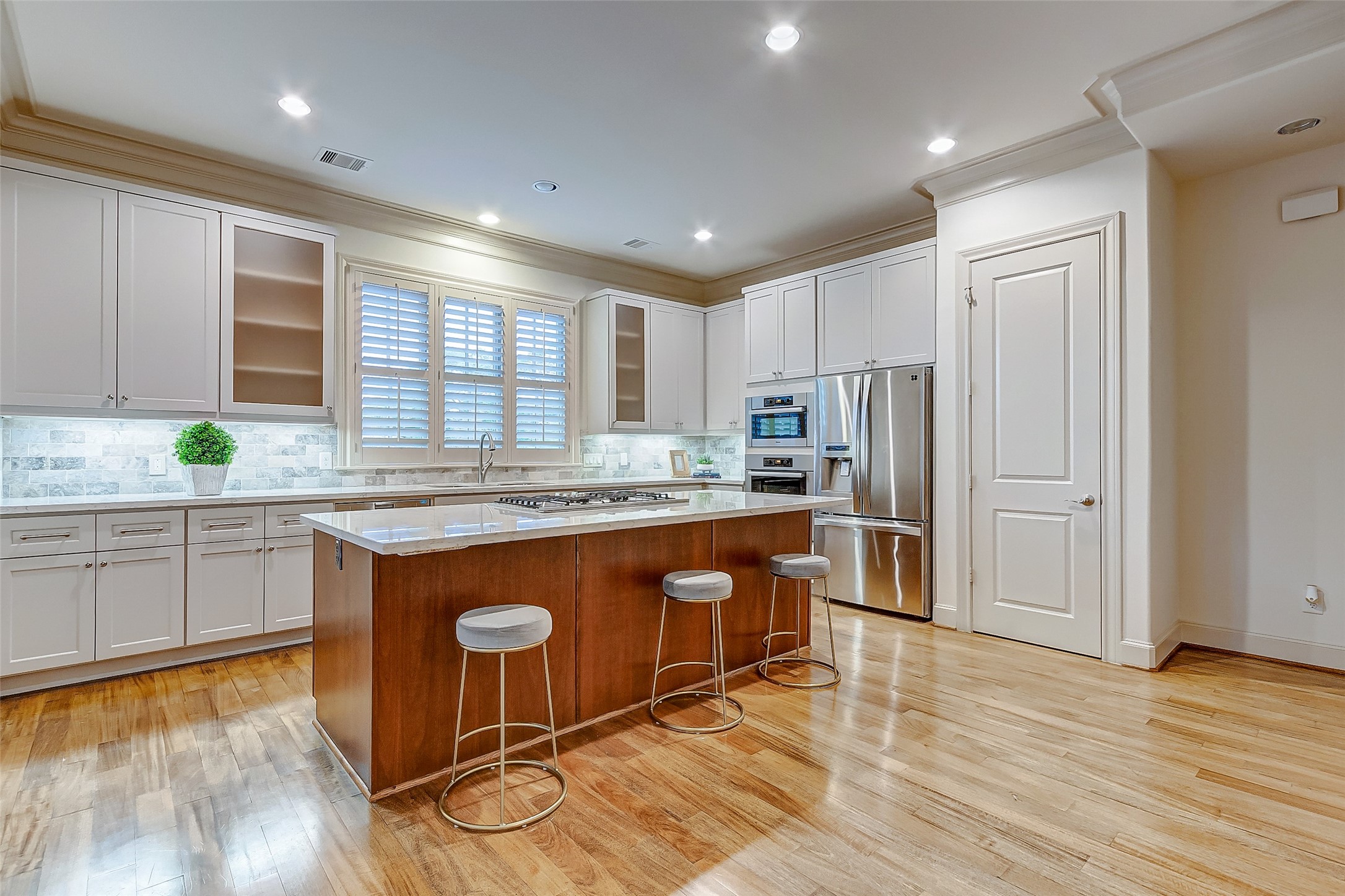 Spacious modern kitchen featuring sleek white cabinetry, a large center island with seating, and stainless steel appliances, all illuminated by recessed lighting.