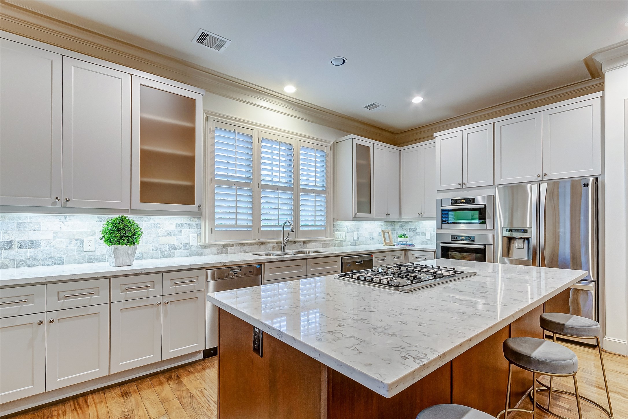 Spacious and modern kitchen featuring sleek white cabinetry, a large marble island with a built-in cooktop, stainless steel appliances, and elegant lighting.