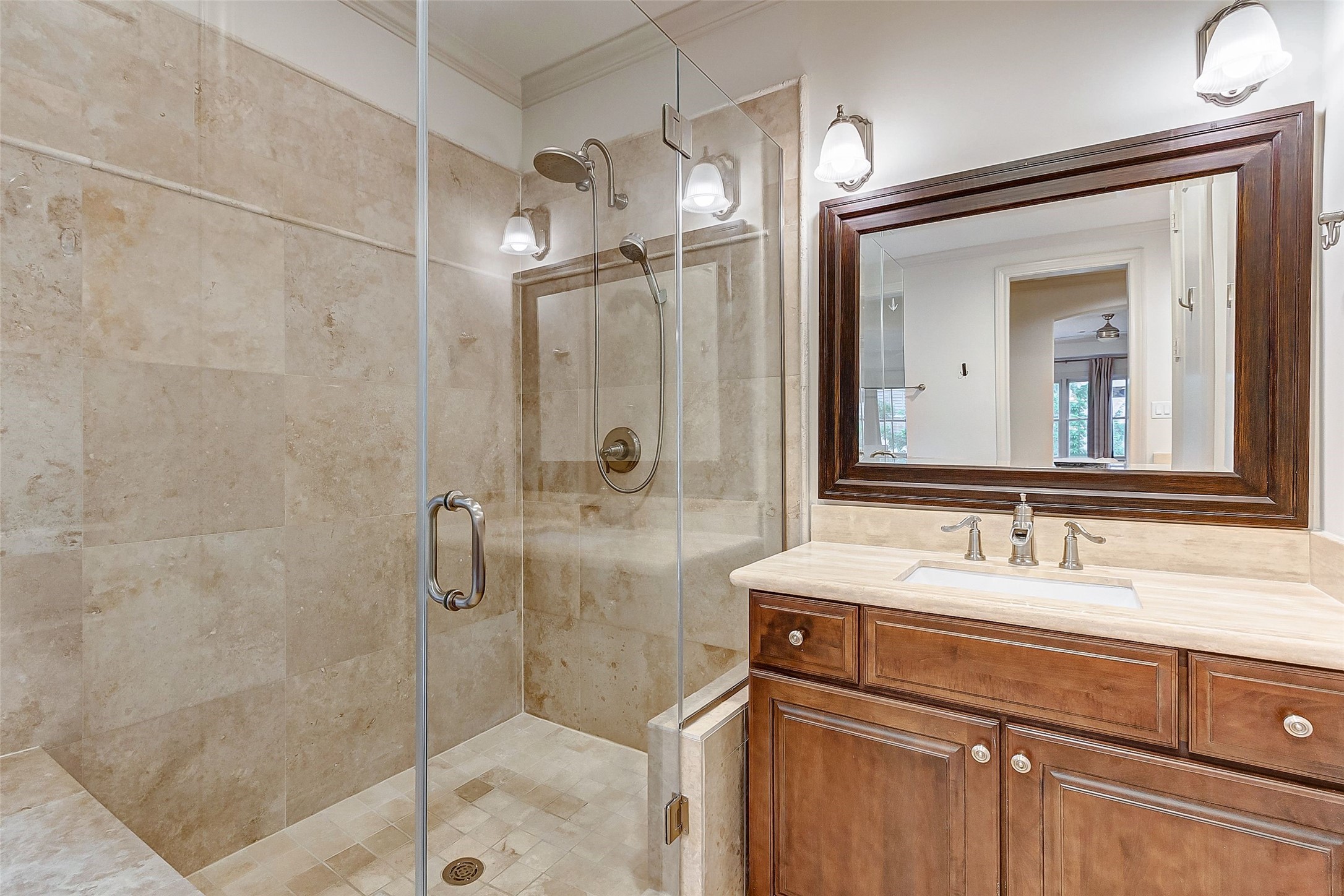 Luxurious bathroom featuring a spacious glass-enclosed shower with elegant tile work, complemented by a sleek vanity with a large framed mirror and modern lighting.