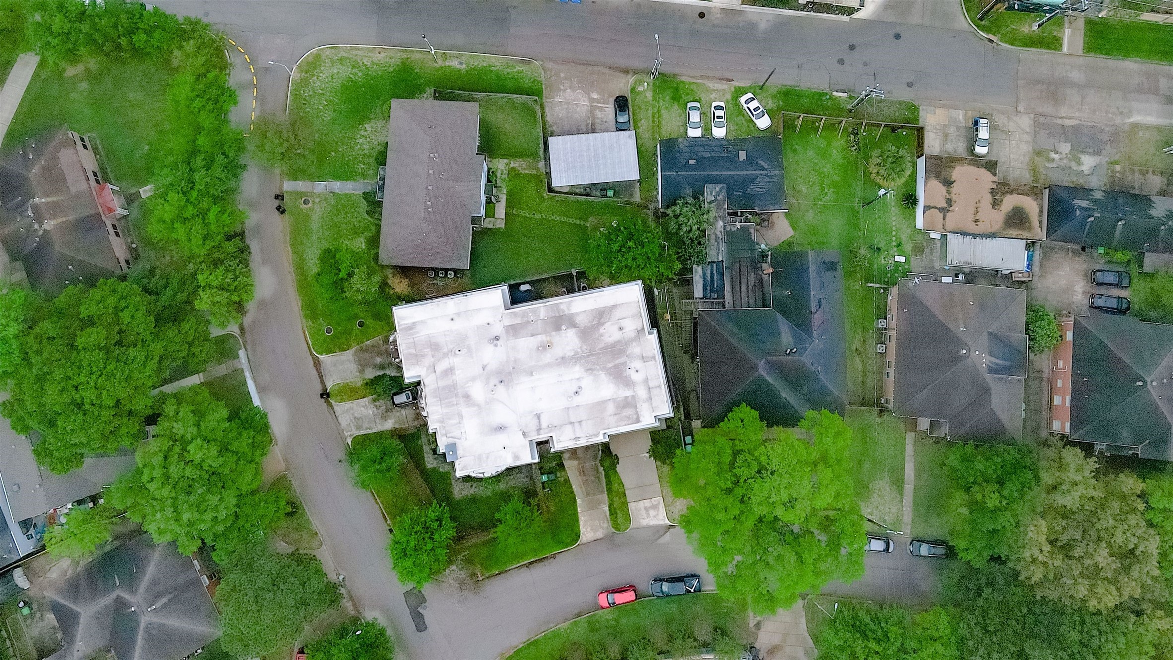 Aerial view showcasing a spacious property with ample greenery, nestled in a quiet residential neighborhood. The home's unique layout offers privacy and a generous driveway.