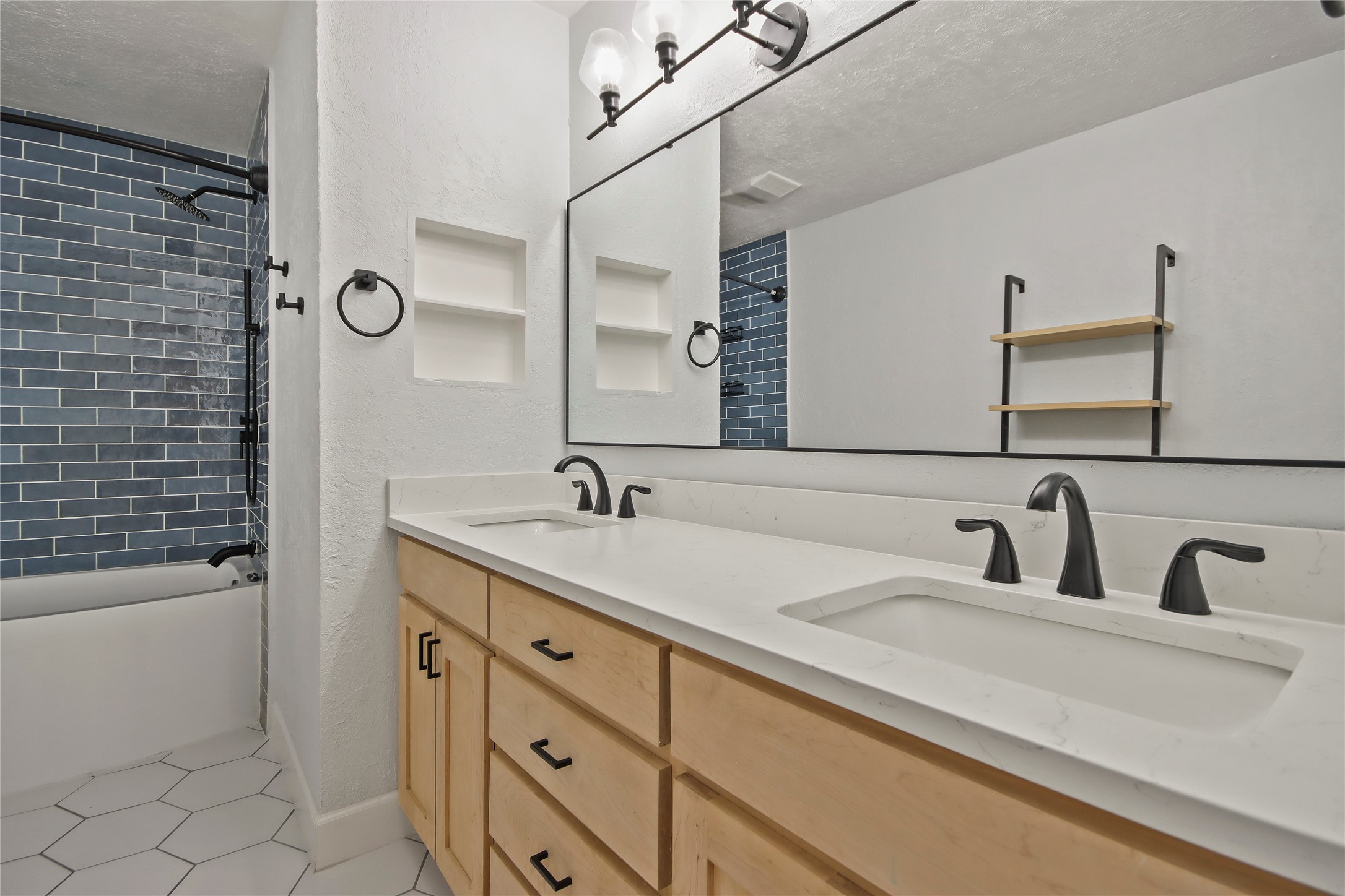 This secondary bathroom features a tub/shower combo with blue subway tile and a quartz-topped dual vanity.