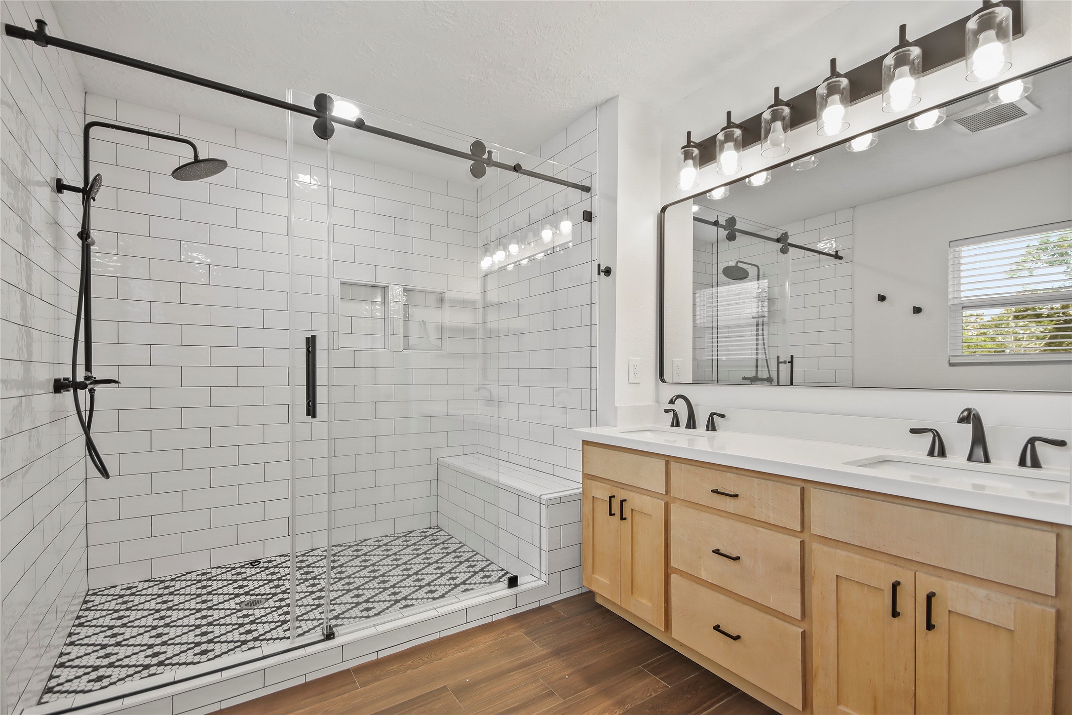 The newly renovated ensuite bath features a barn-door glass shower with subway tile, a built-in bench, and a dual vanity with stylish lighting.