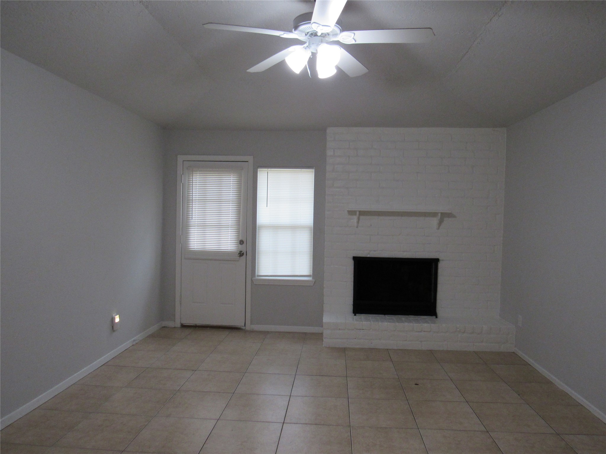 Living room w/ hi ceilings, brick WBPL, lighted fan, and door to backyard.