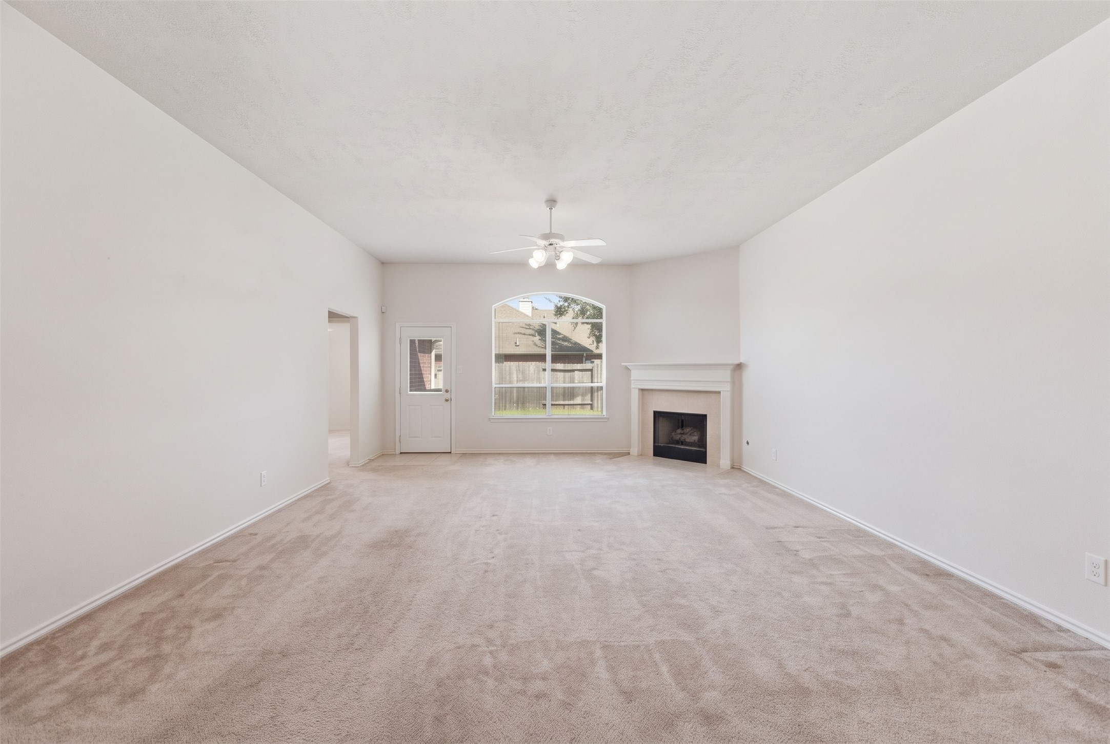 Spacious living room featuring neutral carpeting, a cozy fireplace, and abundant natural light from large windows.