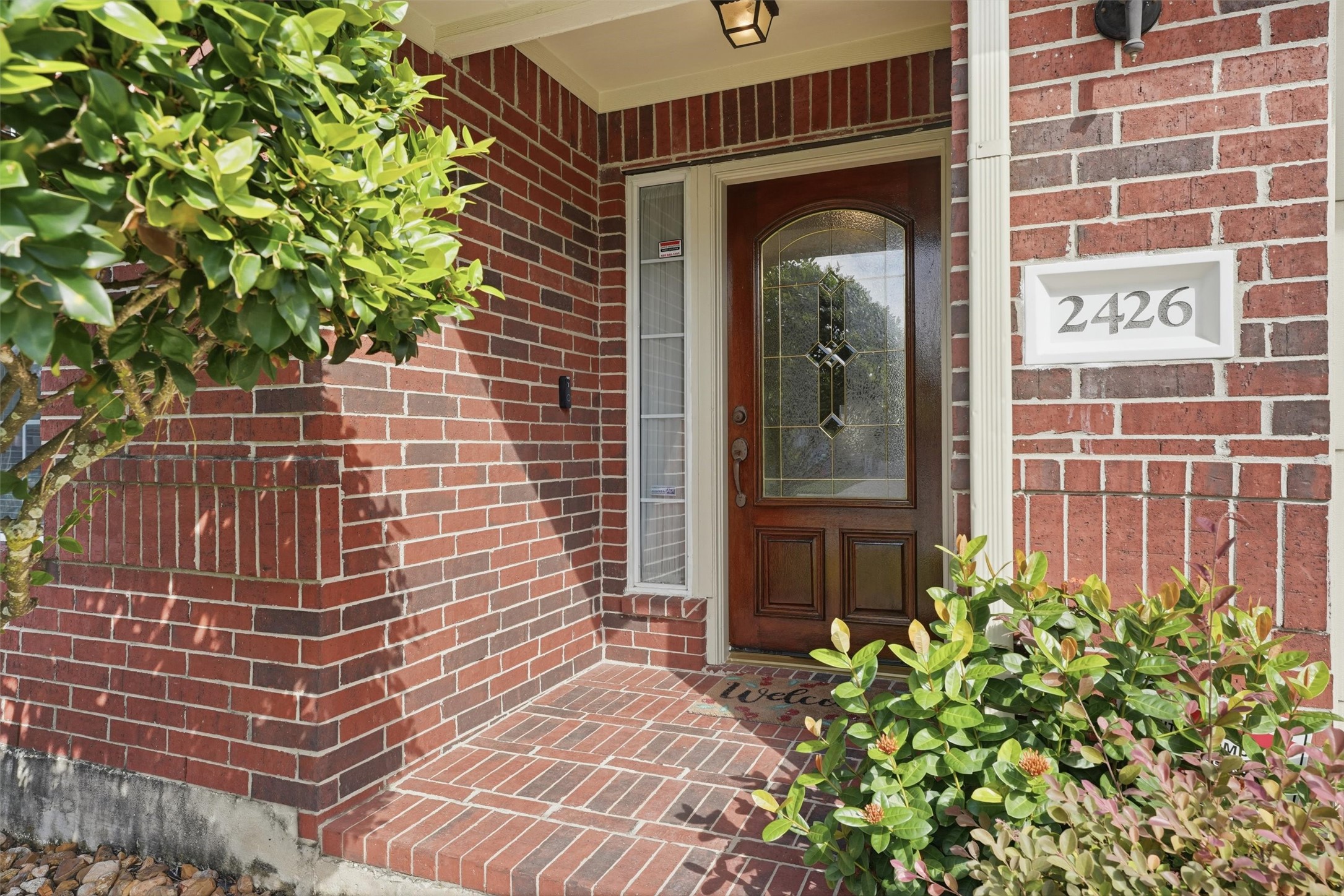 Discover the charm of this inviting front door, beautifully framed by rich brickwork and lush greenery, offering a warm welcome home.