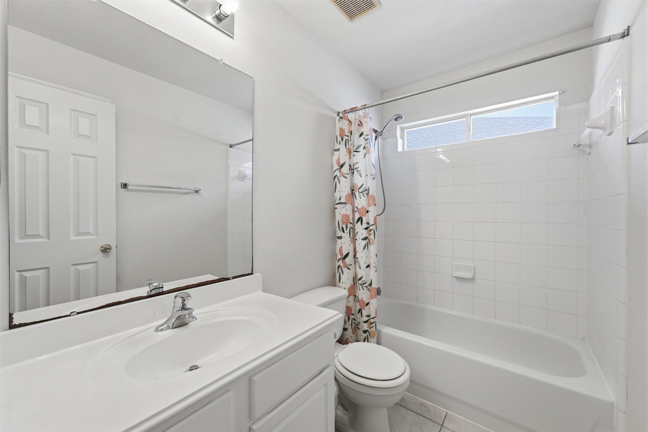 Bright and inviting bathroom featuring a clean, white vanity, spacious mirror, and a tub-shower combination with a floral curtain.