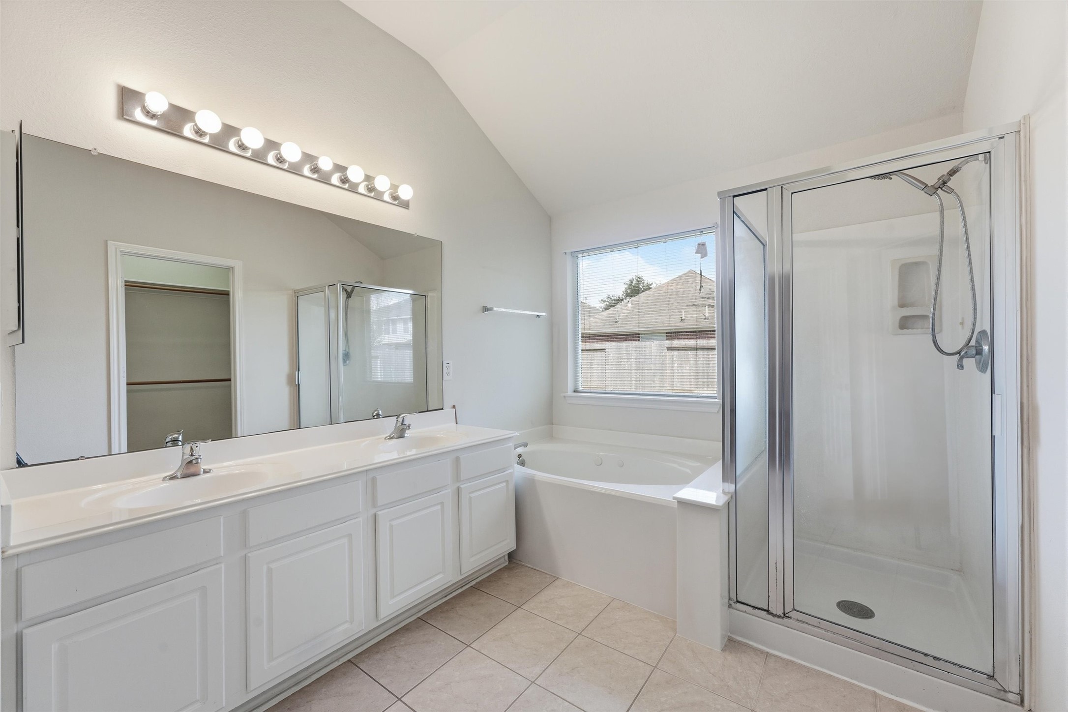 Spacious bathroom featuring a double vanity, large mirror with ample lighting, a relaxing bathtub, and a separate glass-enclosed shower.