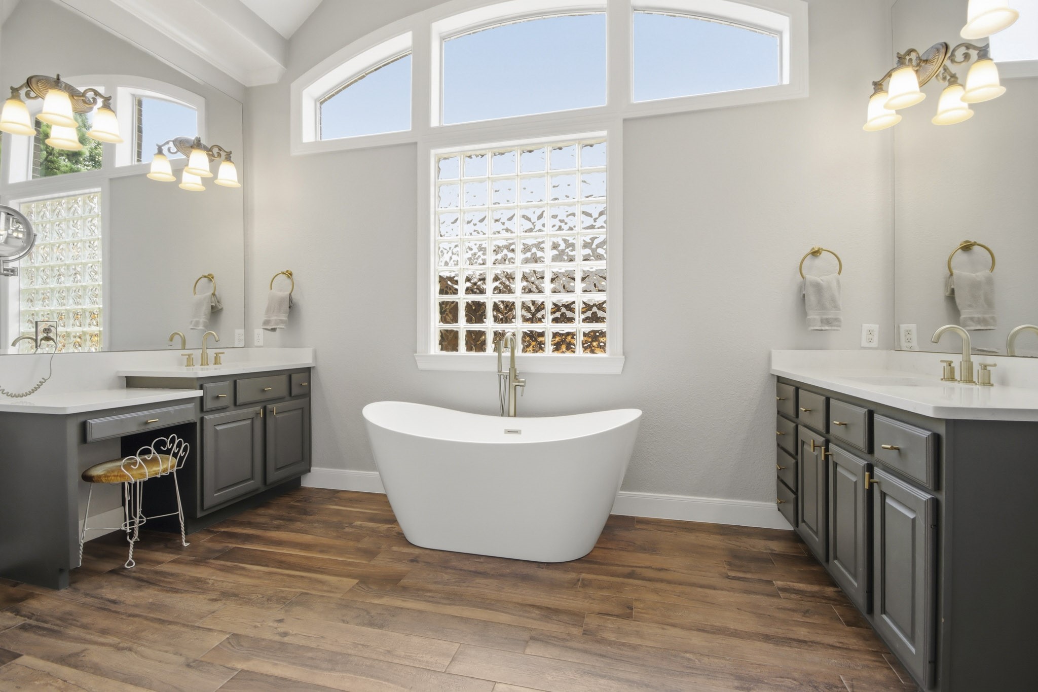 Luxurious bathroom featuring a beautiful freestanding tub, dual vanities with elegant fixtures, and abundant natural light through arched windows.