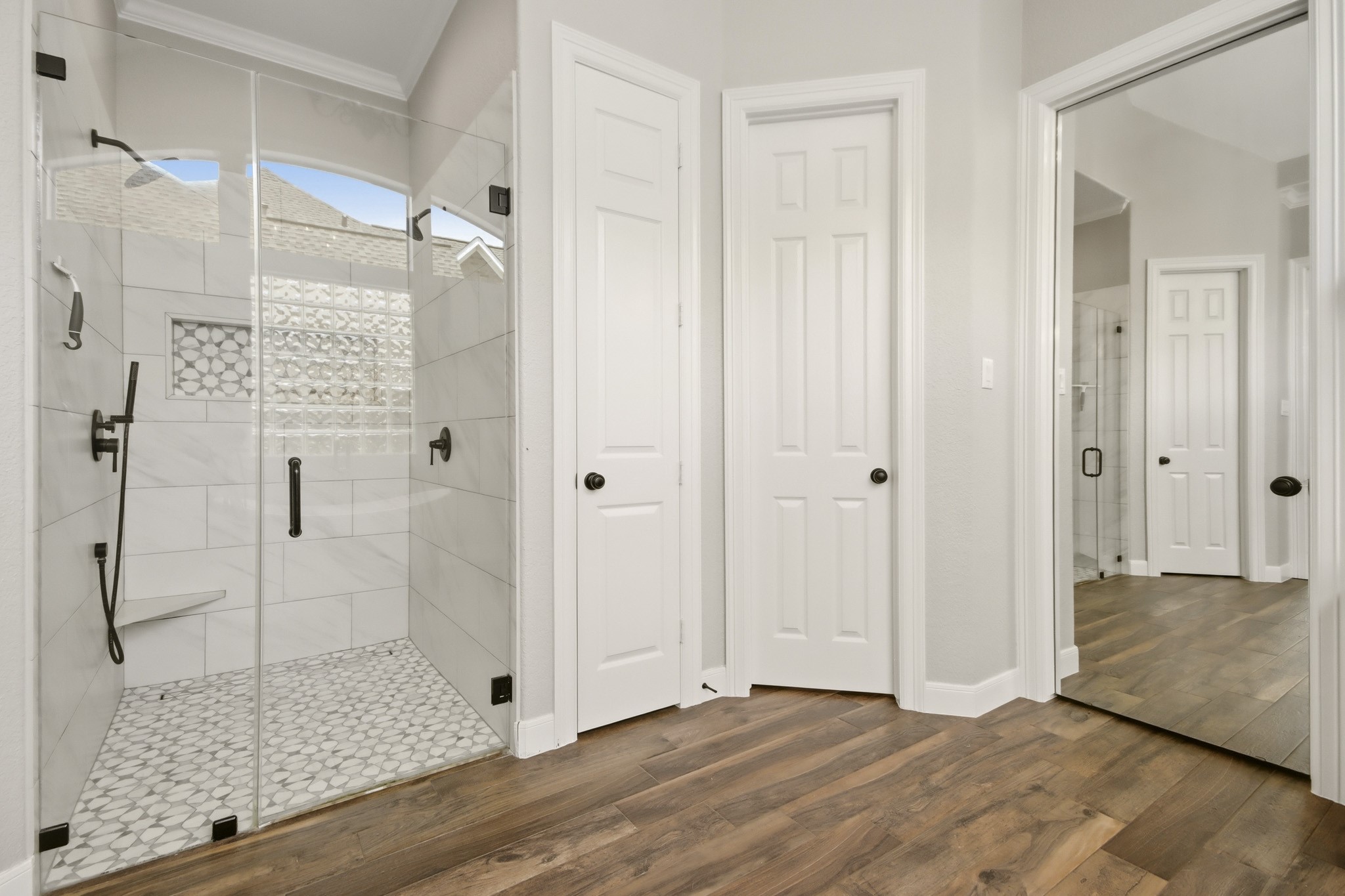 The Primary bathroom includes a spacious glass-enclosed shower with modern fixtures, stylish tile work, and warm wood-like tile flooring.