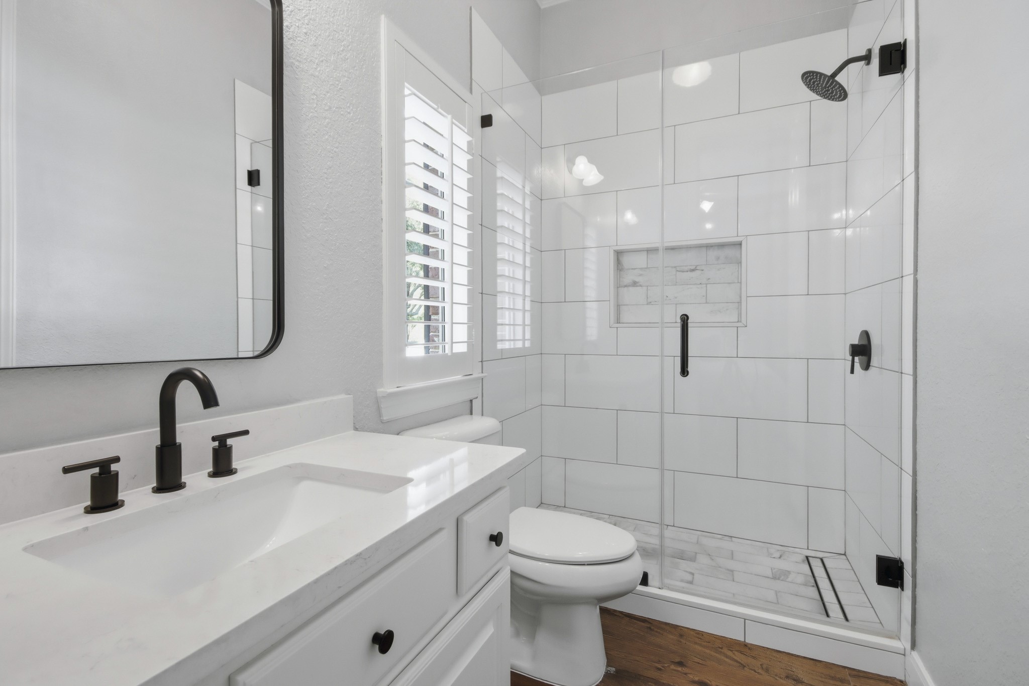 Updated modern downstairs en-suite bathroom featuring a spacious glass-enclosed shower, white tile, and stylish black fixtures for a contemporary touch.