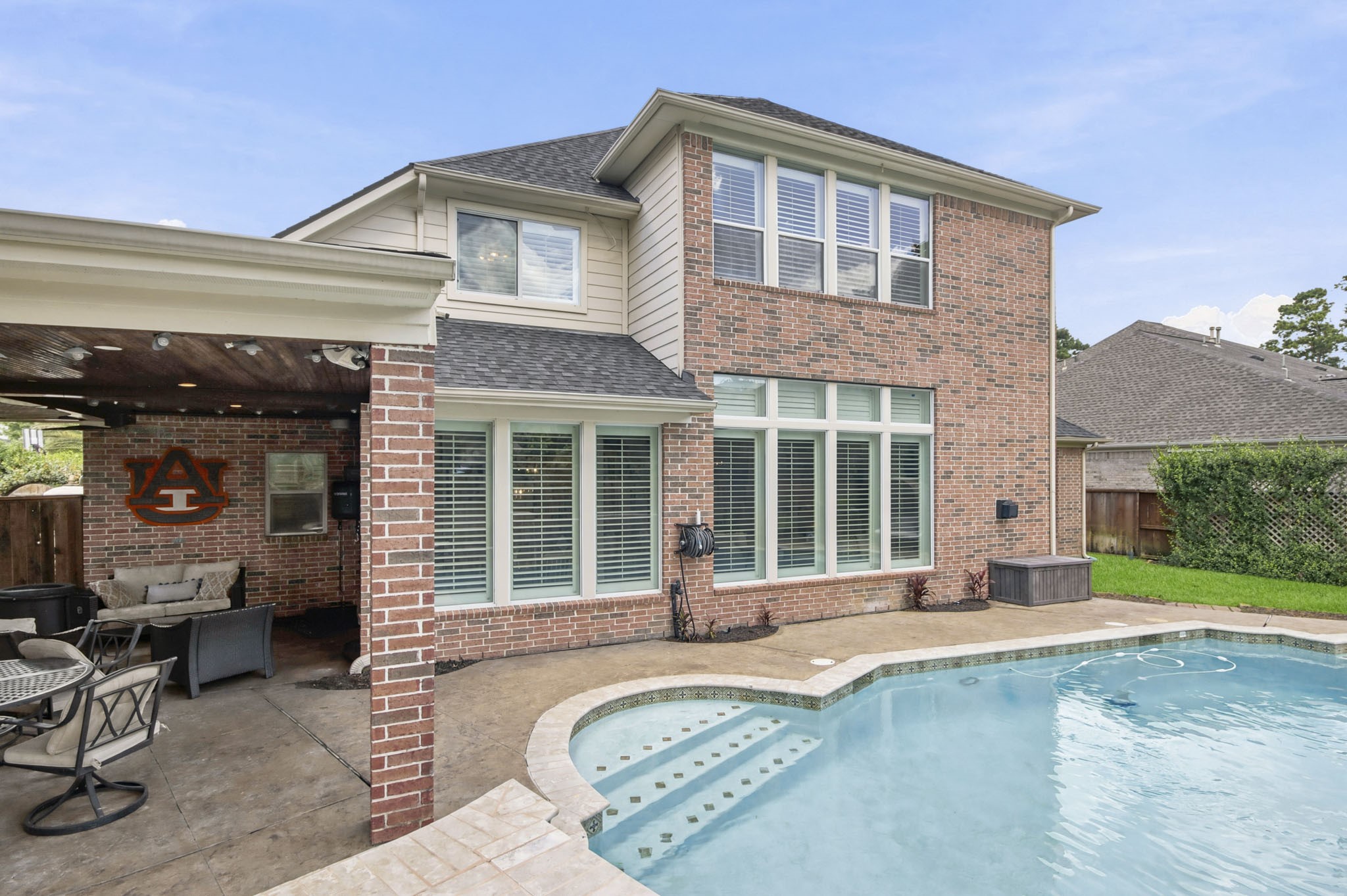 Charming two-story brick home with a refreshing pool and cozy covered patio, perfect for outdoor relaxation and entertaining.