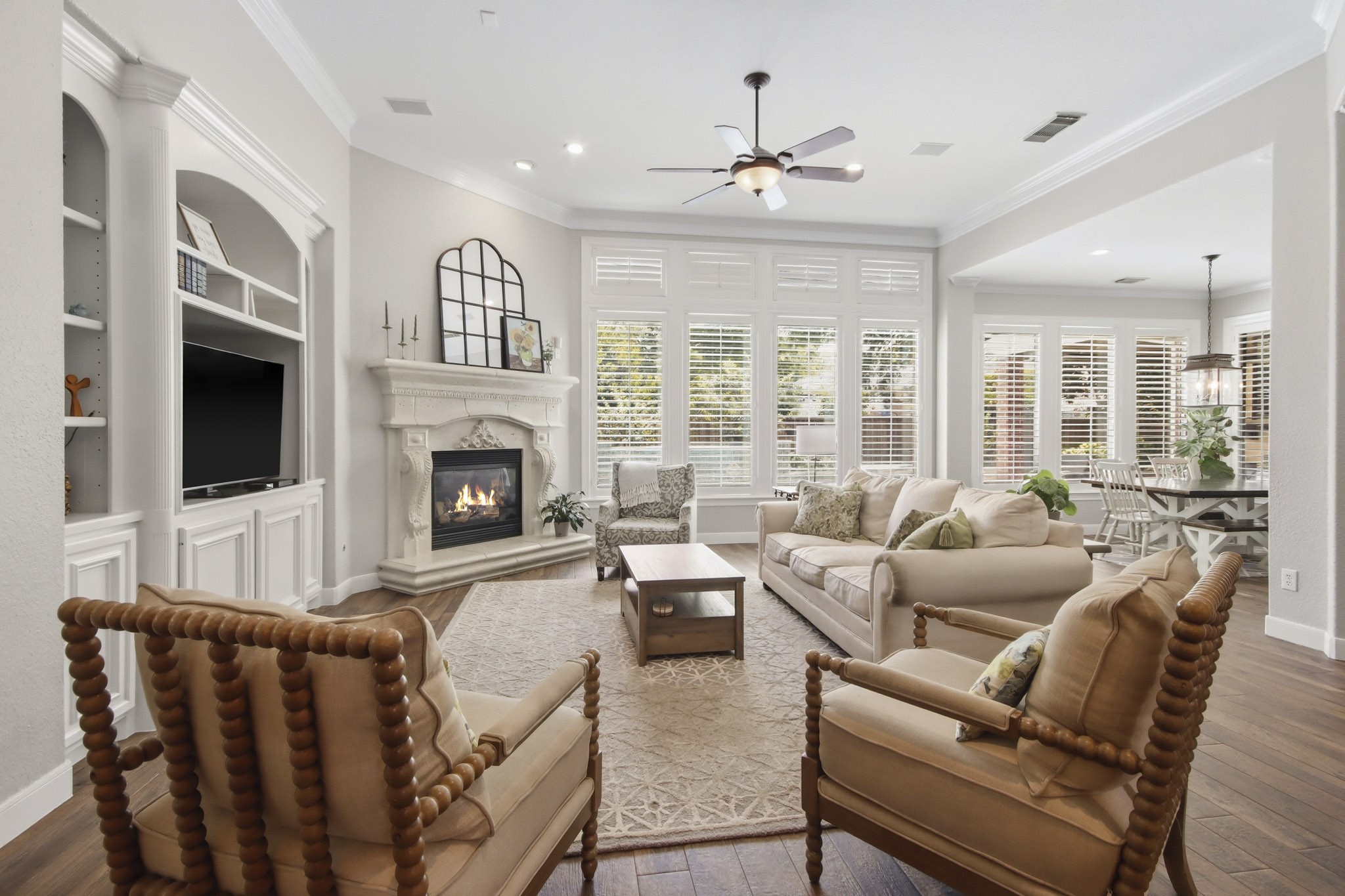 Living room with a cozy fireplace, built-in shelving, and abundant natural light from expansive windows with plantation shutters.
