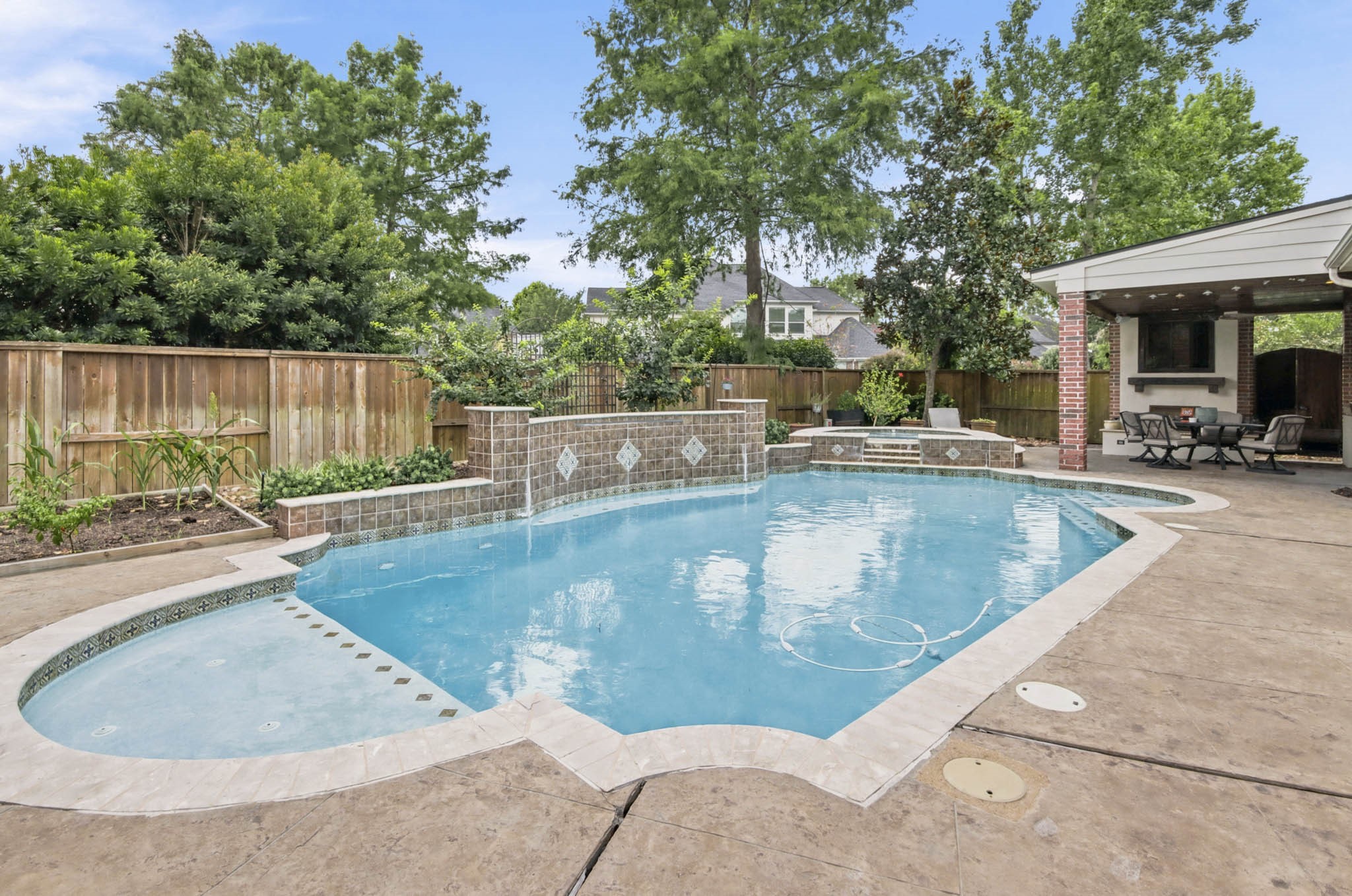 A spacious backyard oasis featuring a sparkling pool with a charming waterfall feature, surrounded by lush greenery and a covered patio perfect for outdoor dining and relaxation.