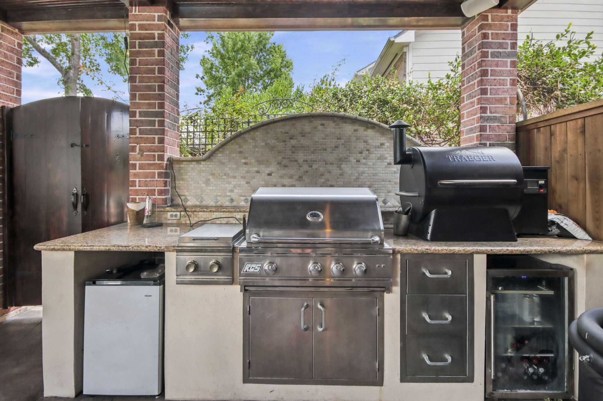 Outdoor kitchen with stainless steel grill, and mini fridge, set against a stylish stone backsplash and brick accents, perfect for entertaining.