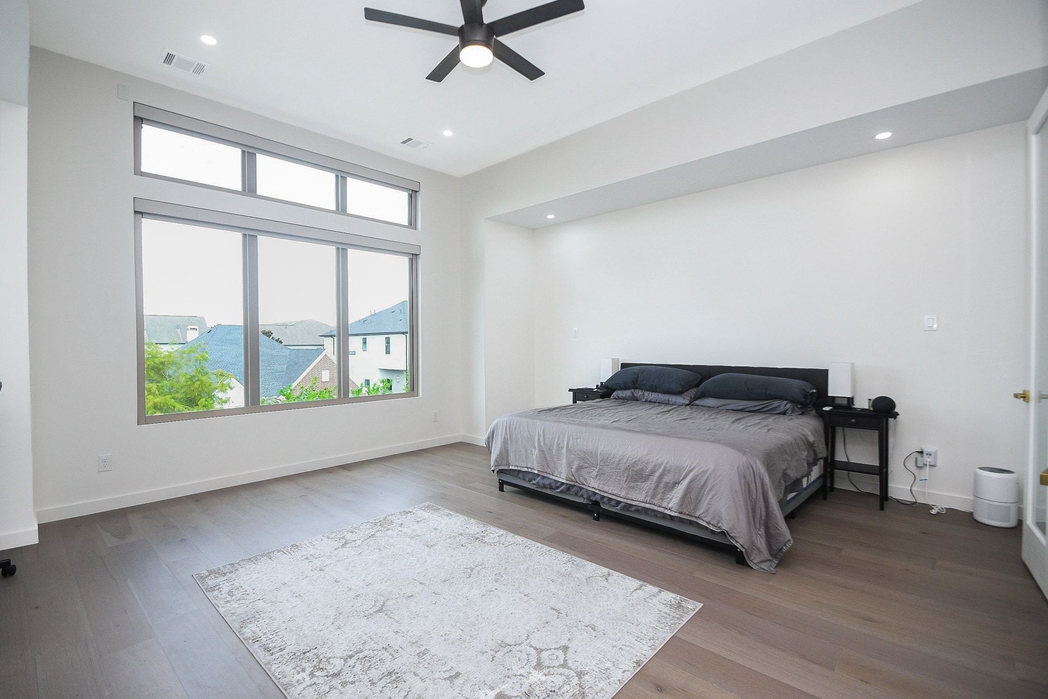 A totally masterful primary suite is complemented by tremendous natural light, via the triple panel wall wide window (left), simple engineered wood flooring, plentiful wall/floor space, embraced by the partial tray ceiling and recessed lighting above to create any mood or rhythm you like!