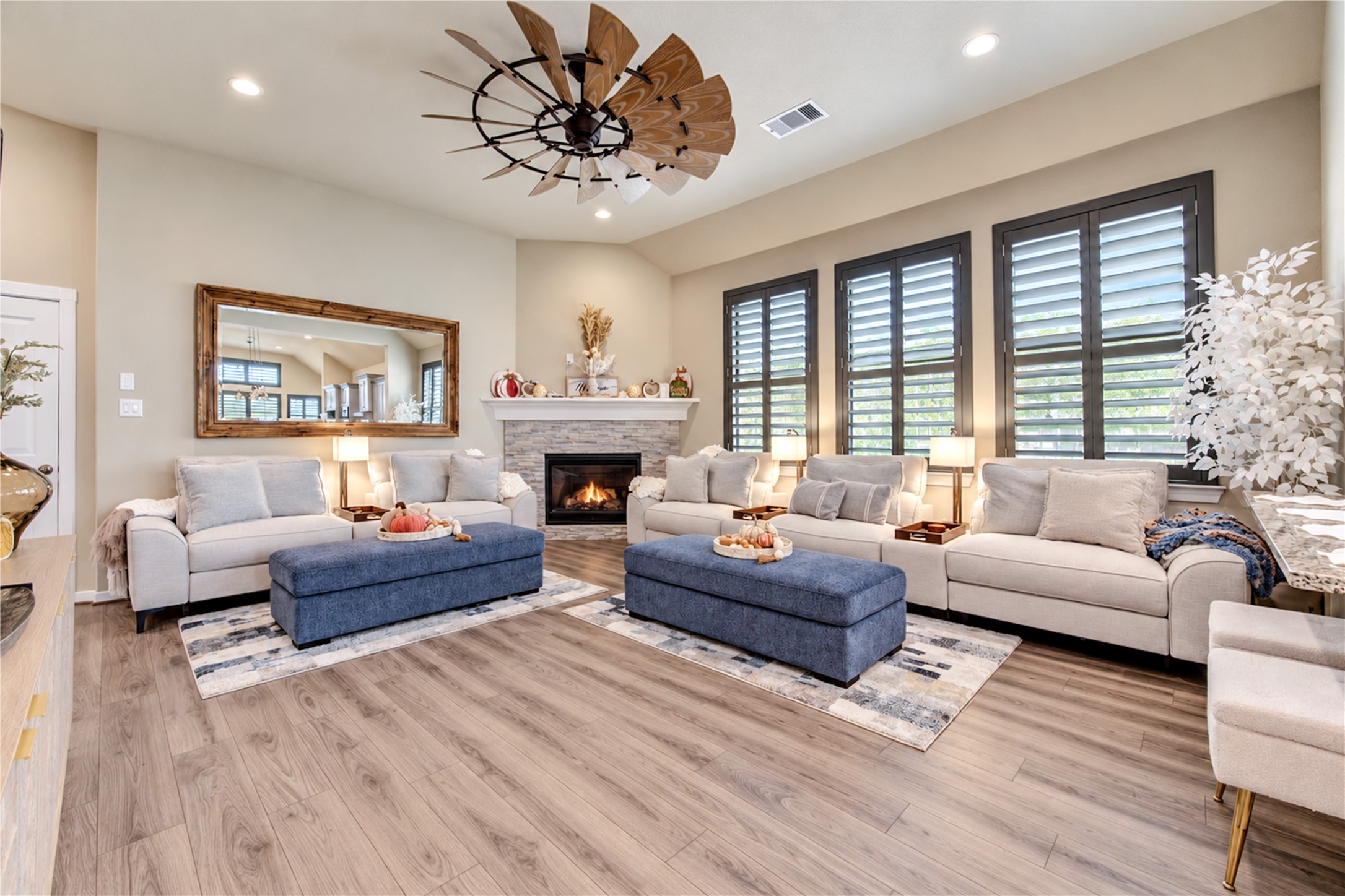 A spacious family room featuring high ceilings, a stone-accented fireplace, plantation shutters and beautiful wood-look tile flooring.