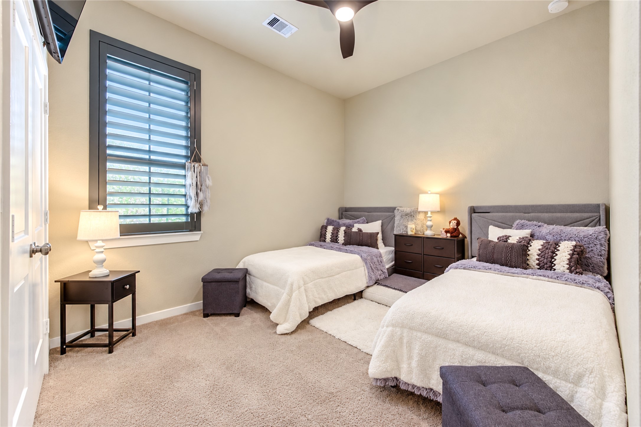 A comfortable secondary bedroom with high ceilings, soft carpeting and a window with plantation shutters.