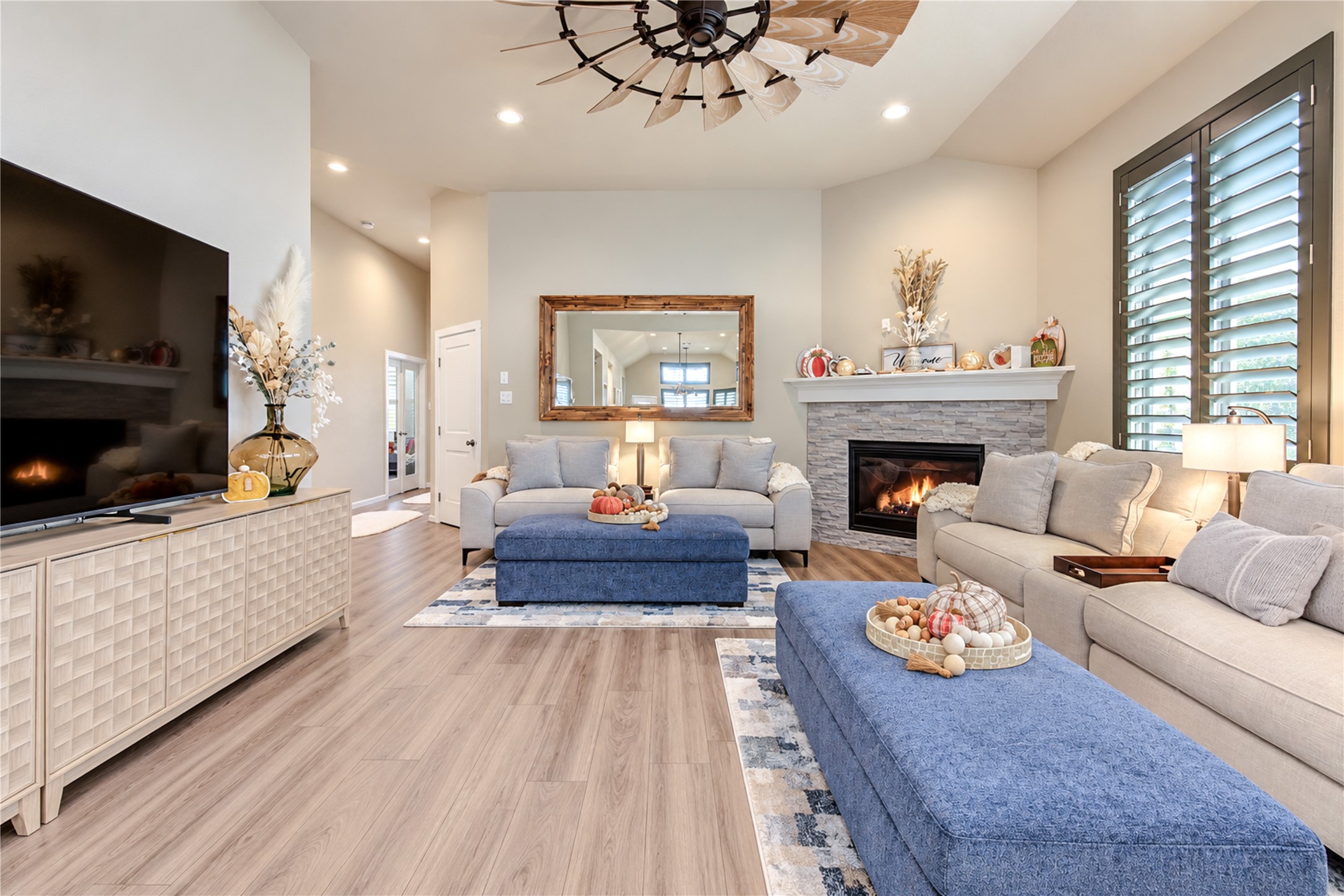 A warm and inviting family room with high ceilings, a beautiful stone-accented fireplace and wood-look tile flooring.