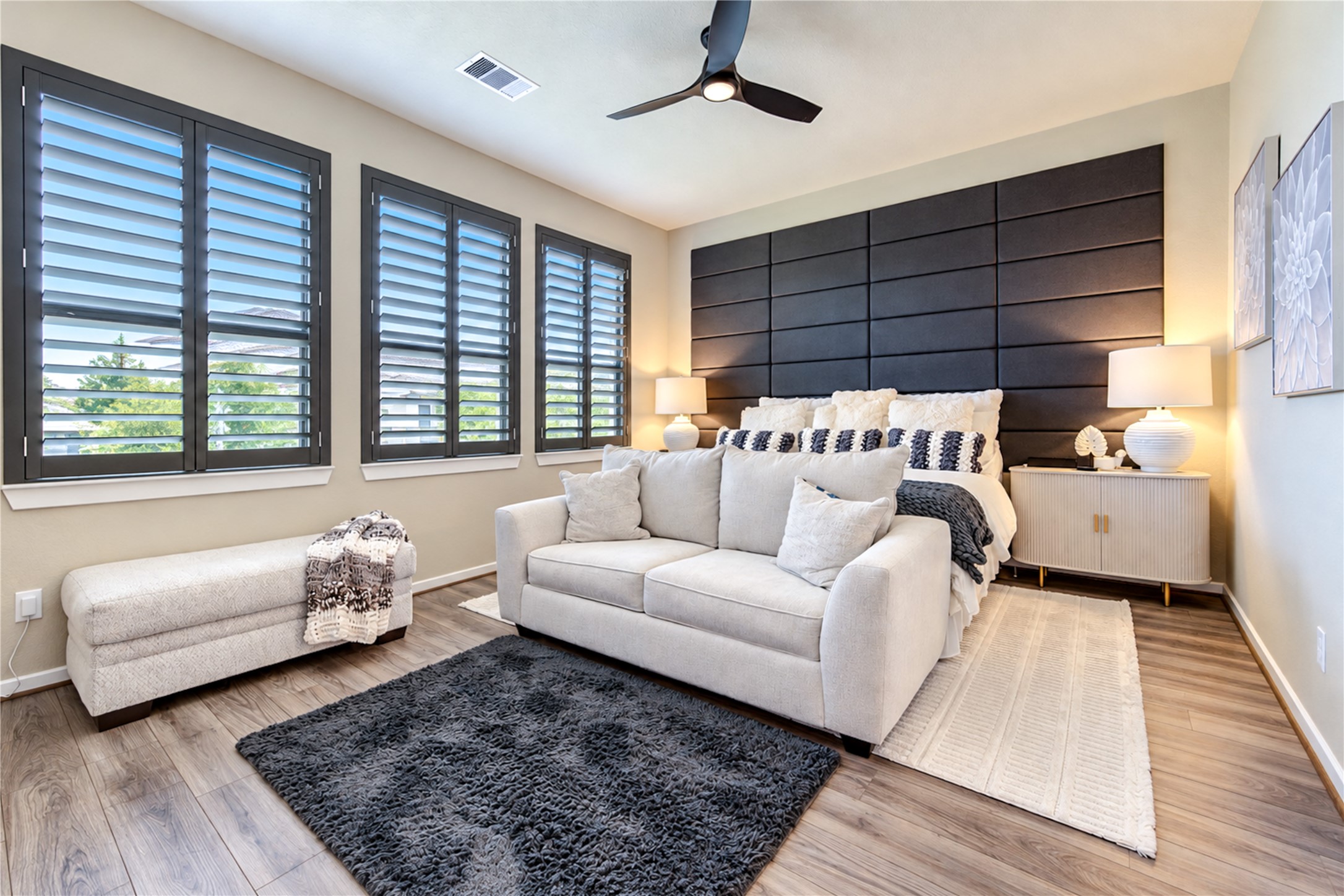 A spacious primary bedroom with wood-look tile flooring, plantation shutters and plenty of natural light.
