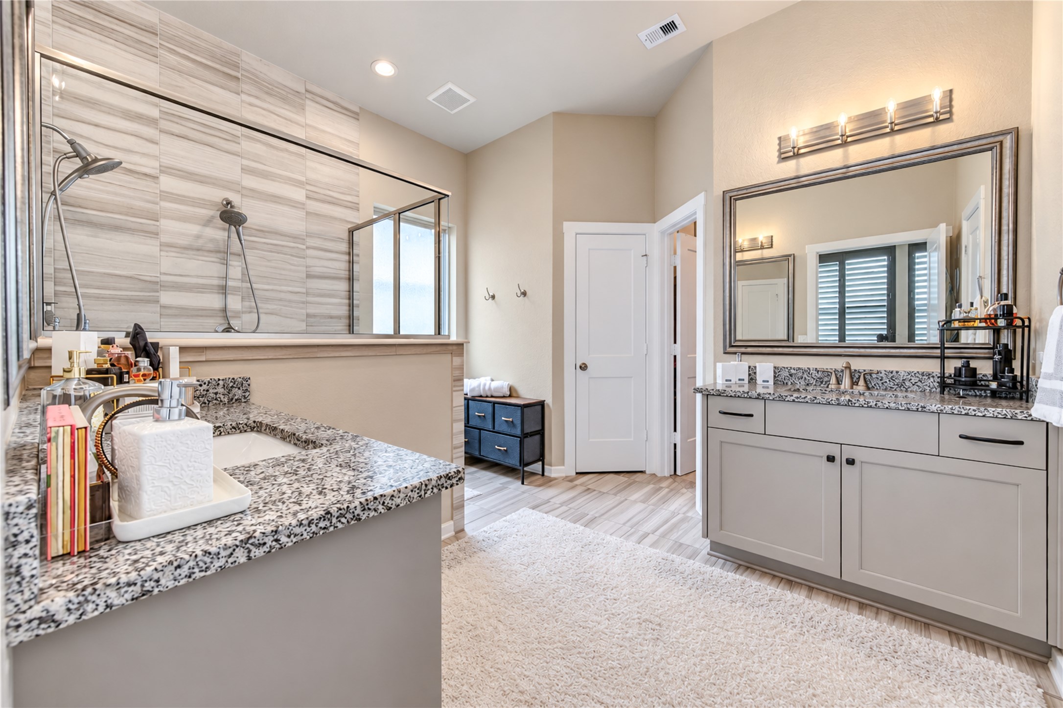 A spacious primary bath featuring separate vanities, granite countertops and a beautifully tiled walk-in shower.