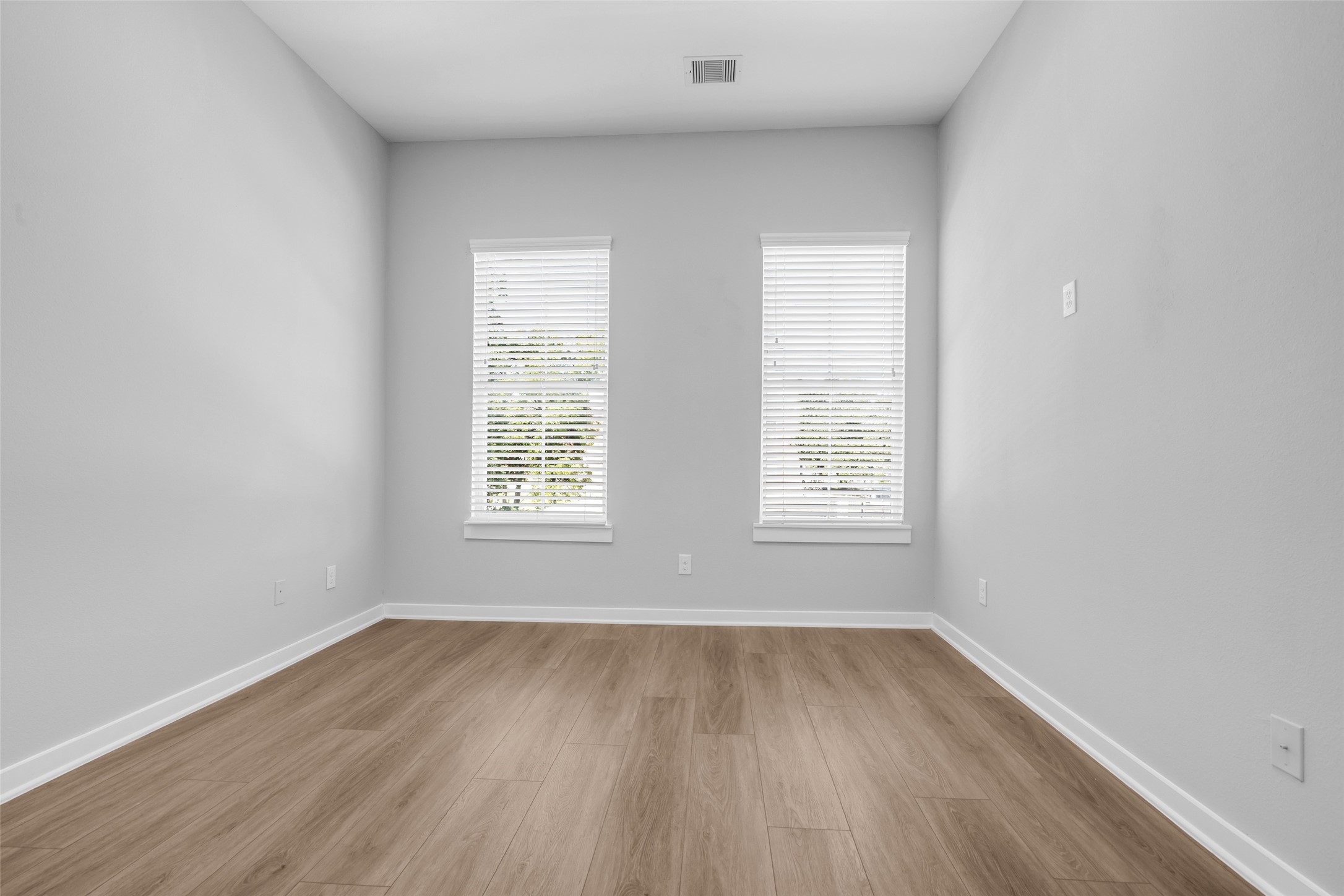 A bright secondary bedroom with two windows, ready for guests or a home office.