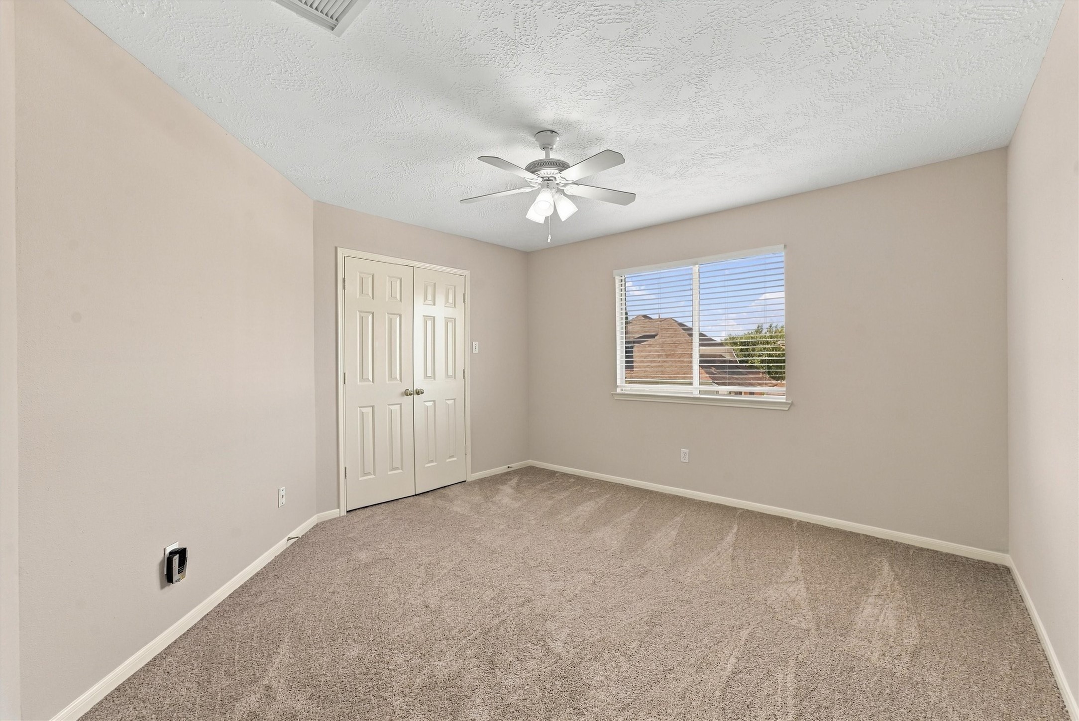 Bright and inviting bedroom featuring soft carpeting, a ceiling fan, and ample natural light from a large window with a pleasant view.