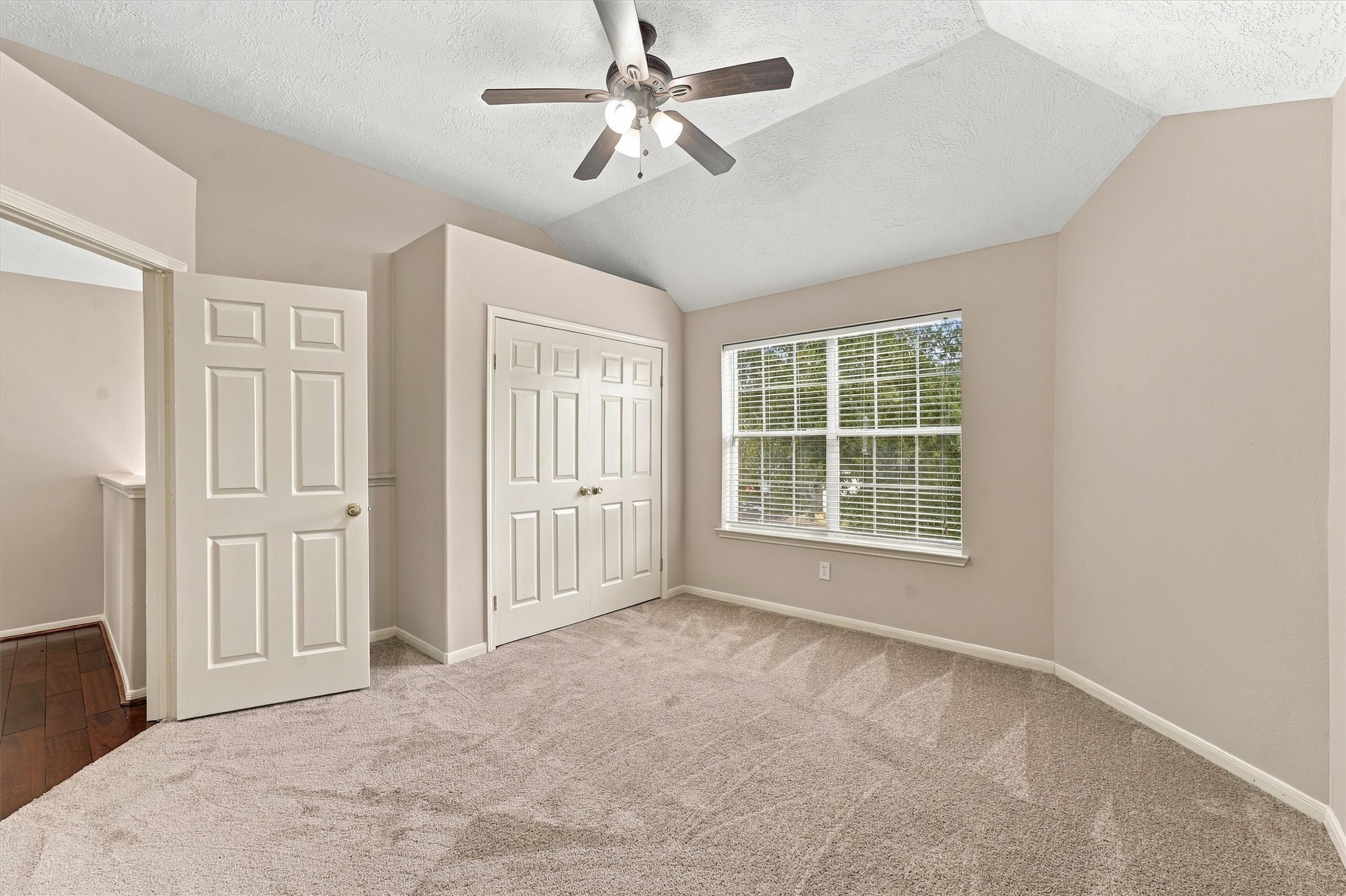 Bright and inviting bedroom featuring plush carpeting, a ceiling fan, and ample natural light from a large window, complemented by double-door closet space.