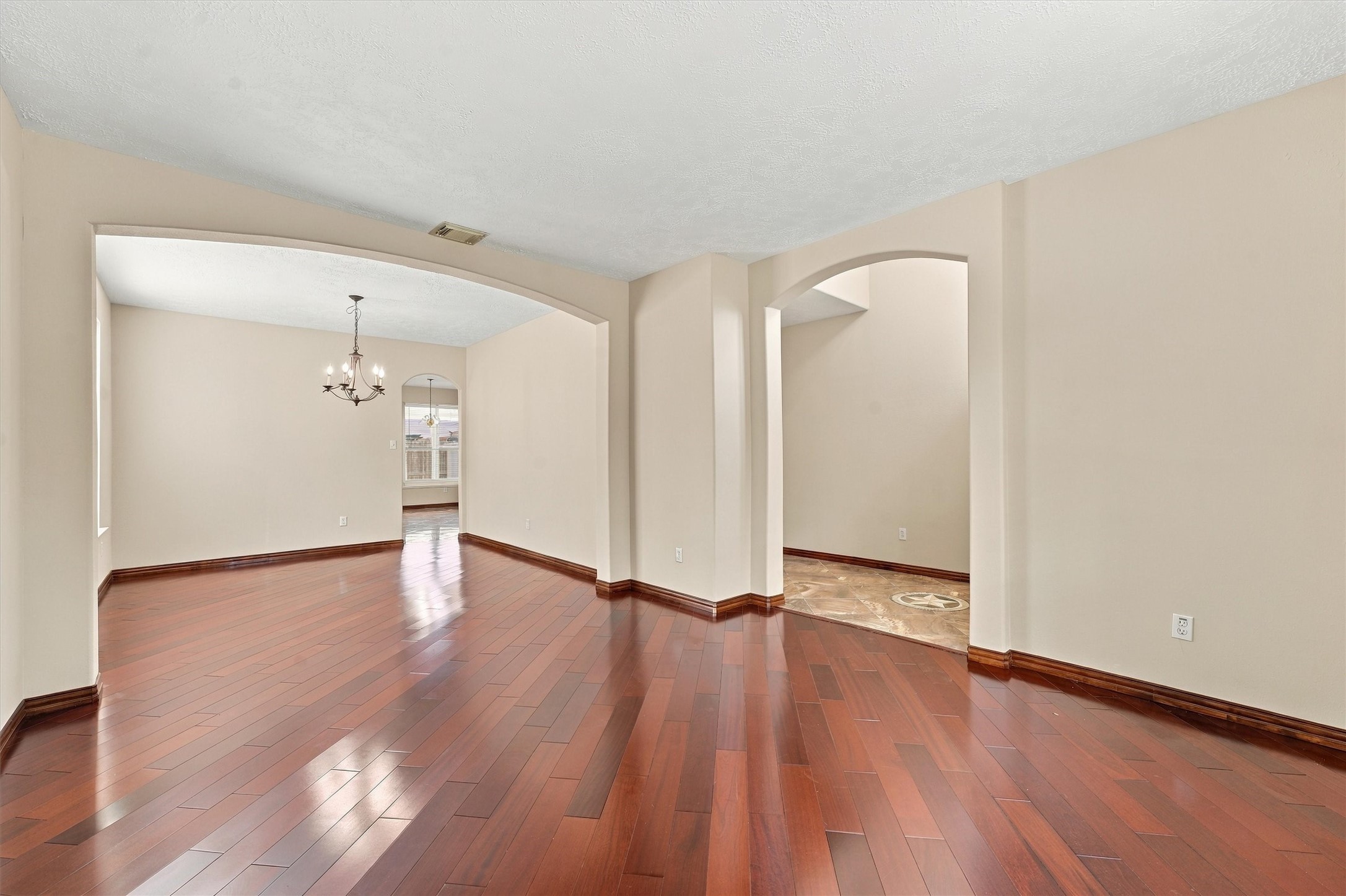 Elegant open-concept living area featuring rich hardwood floors, archways, and a stylish chandelier, perfect for entertaining and family gatherings.