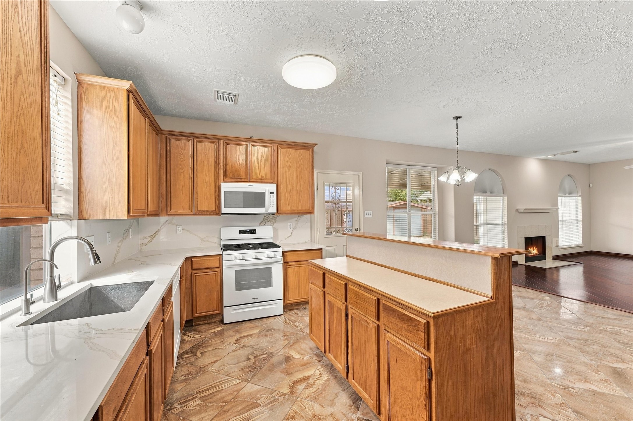 Spacious kitchen with warm wood cabinetry, sleek countertops, and modern appliances, seamlessly flowing into a cozy living area with a charming fireplace.